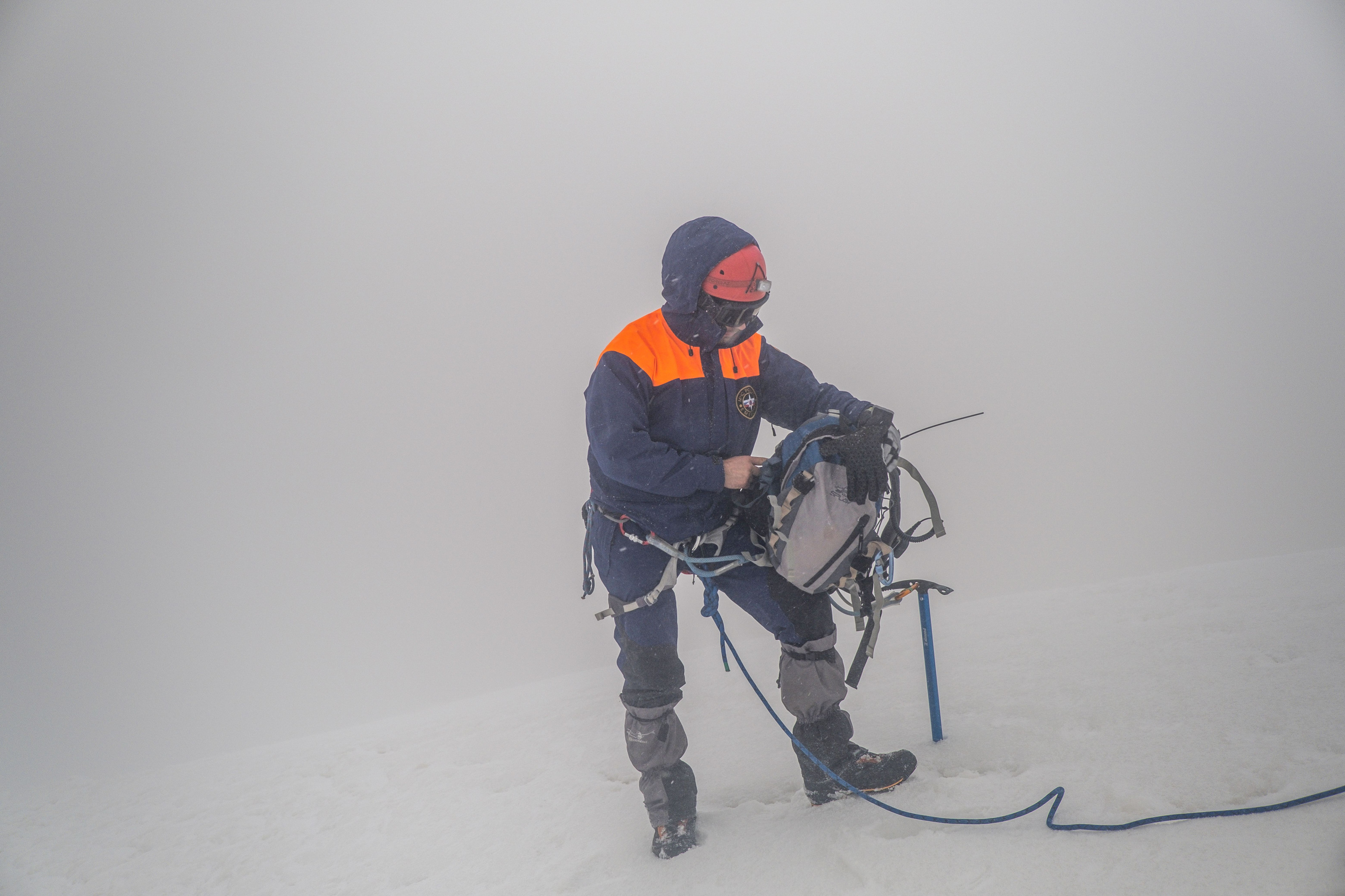 A climber adjusting gear amid snowy, foggy mountain conditions.