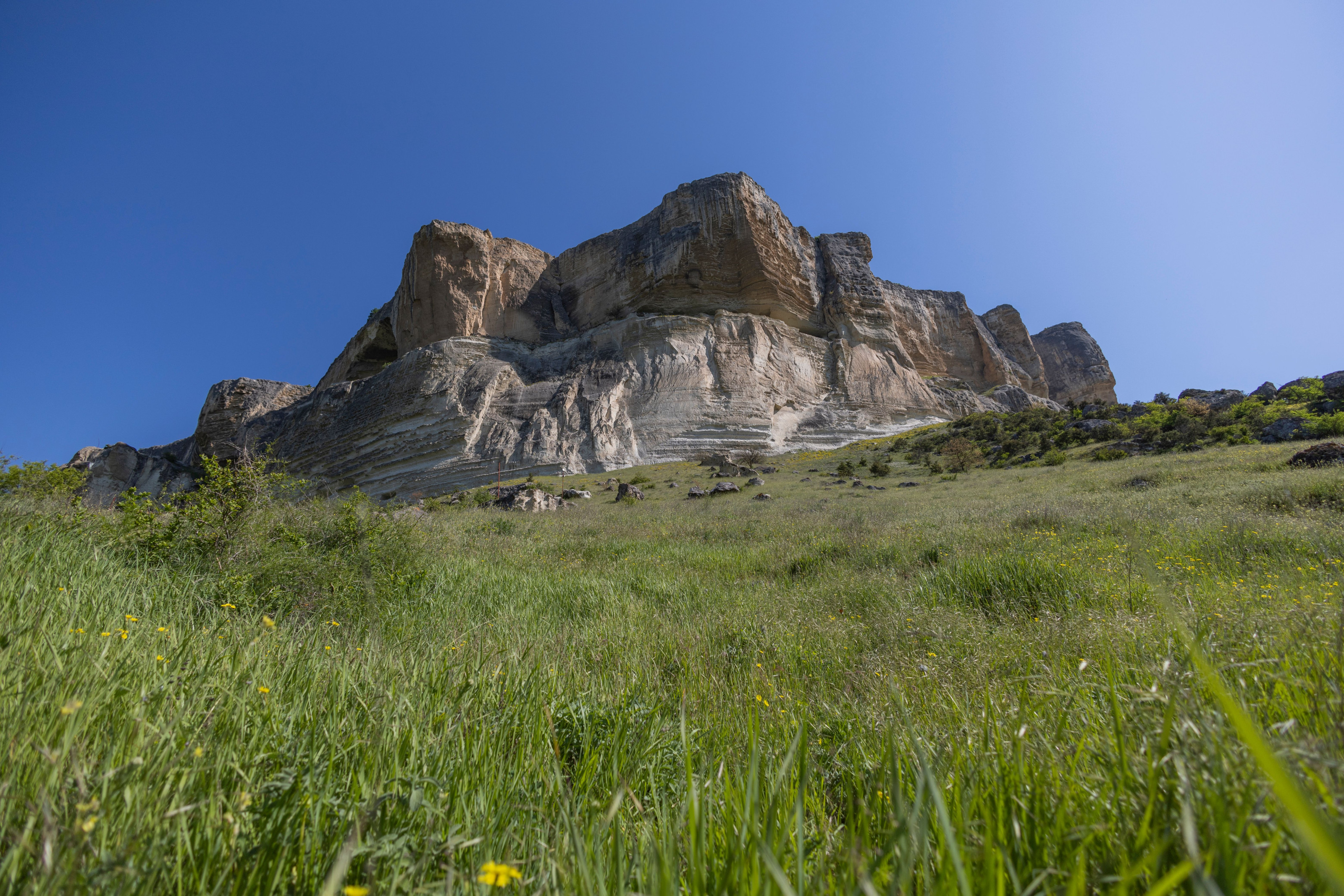 A dramatic rocky ridge rises above a green highland meadow under a clear sky.