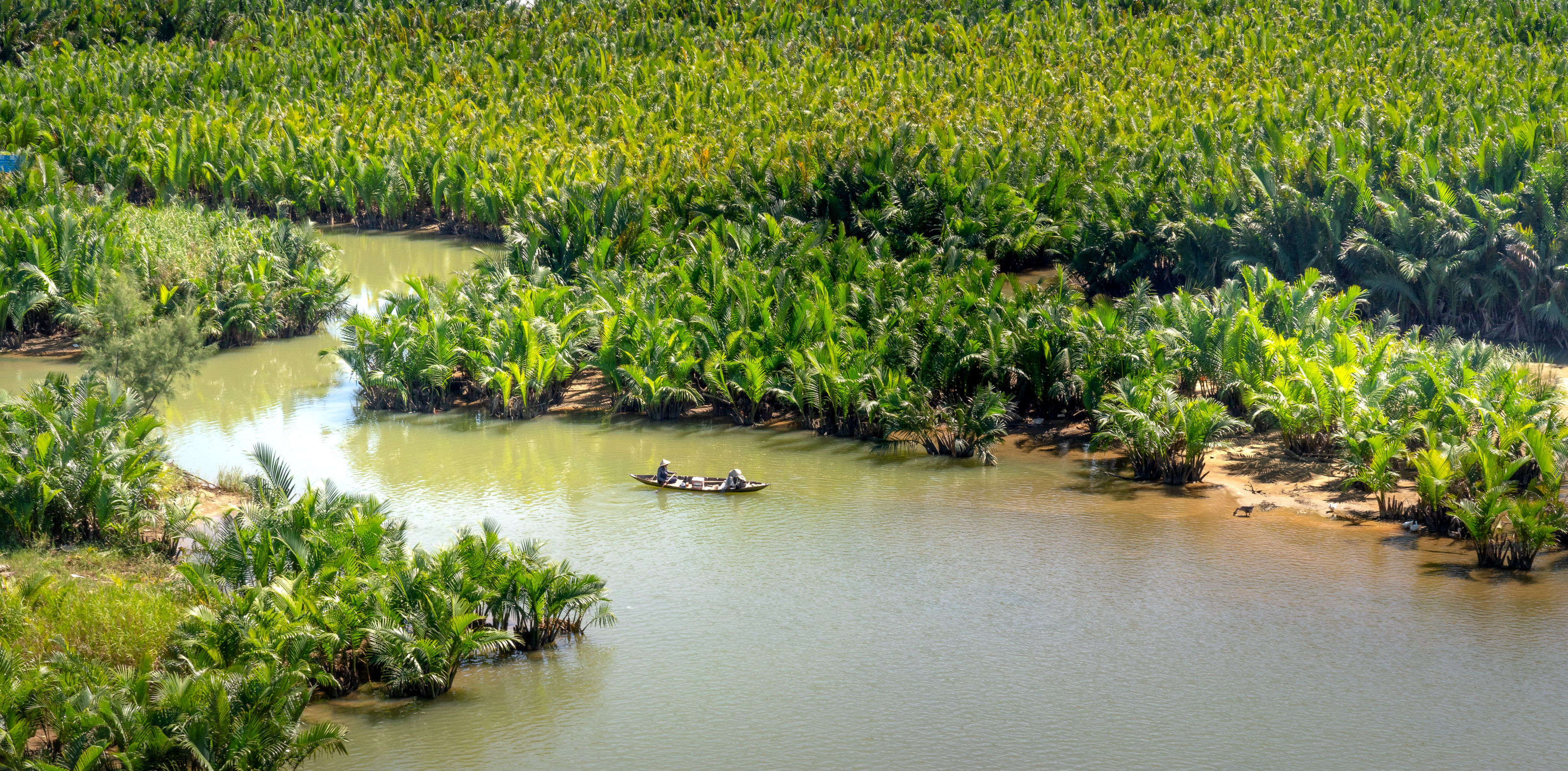 A small boat carries passengers along a calm river bordered by lush greenery.