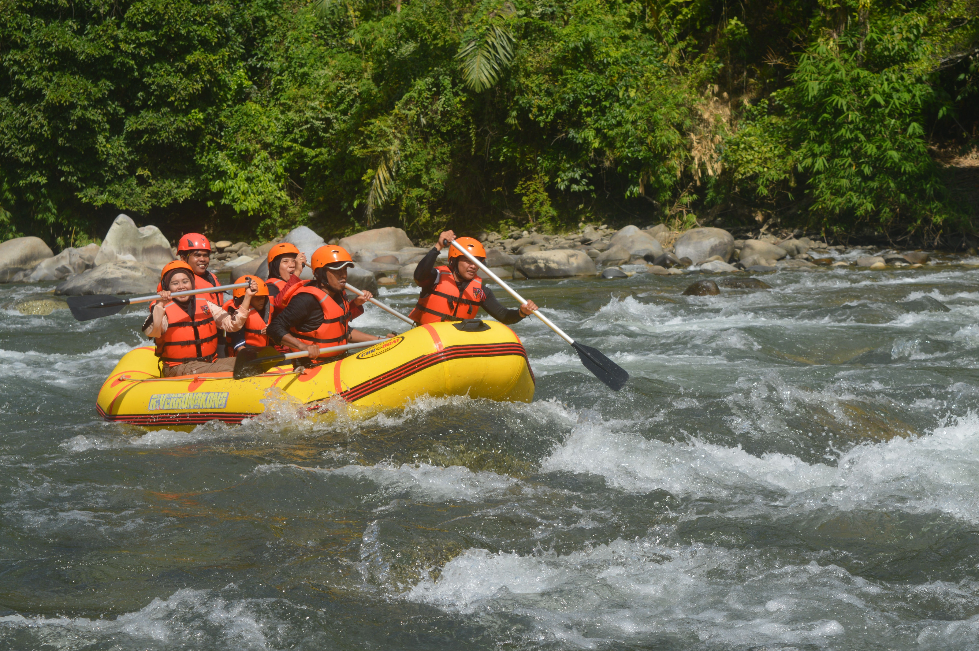 A group of adventurers paddles a raft through a fast-moving river bordered by forest.