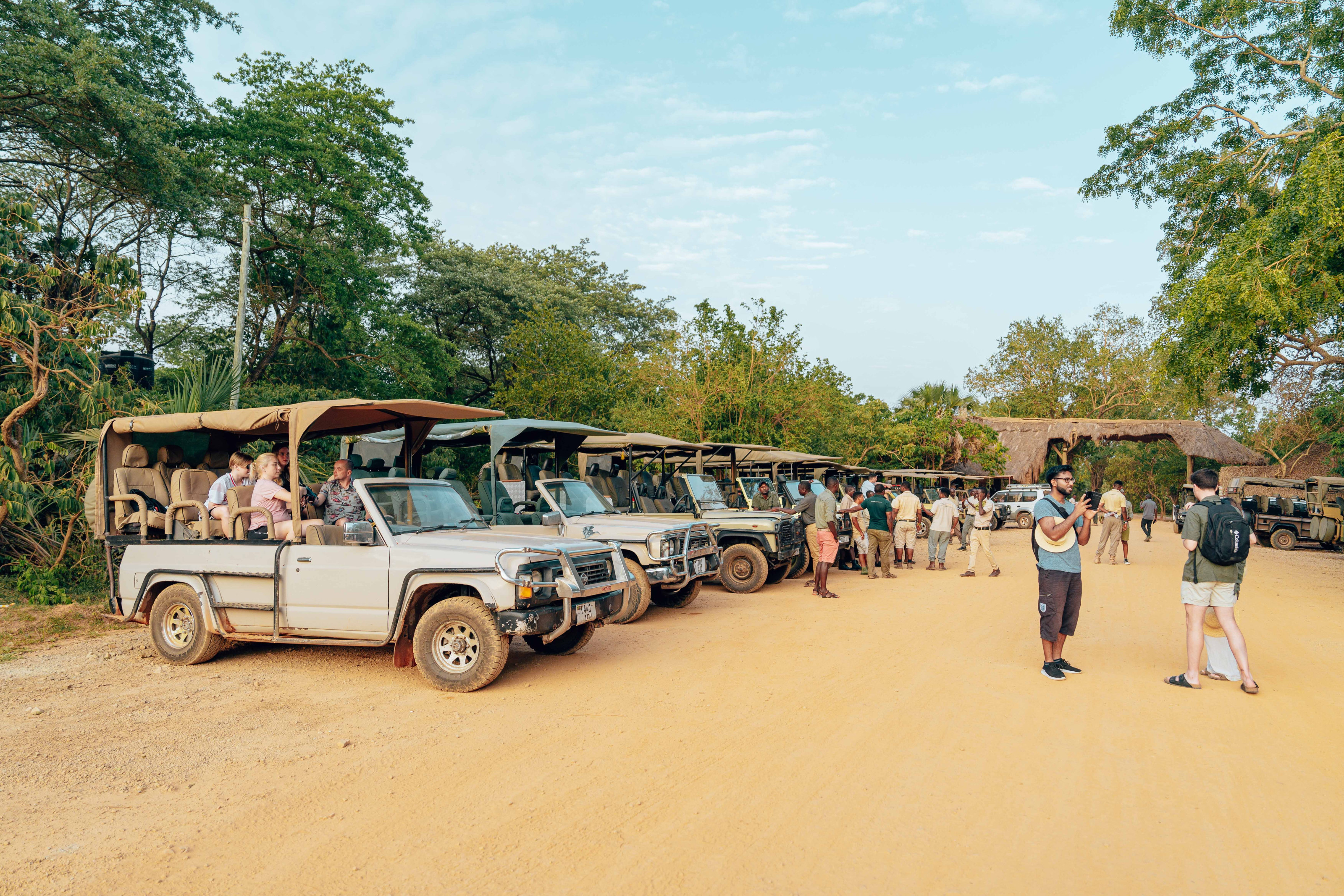 Safari-goers gather beside open-top 4x4 vehicles before setting out on a game drive.