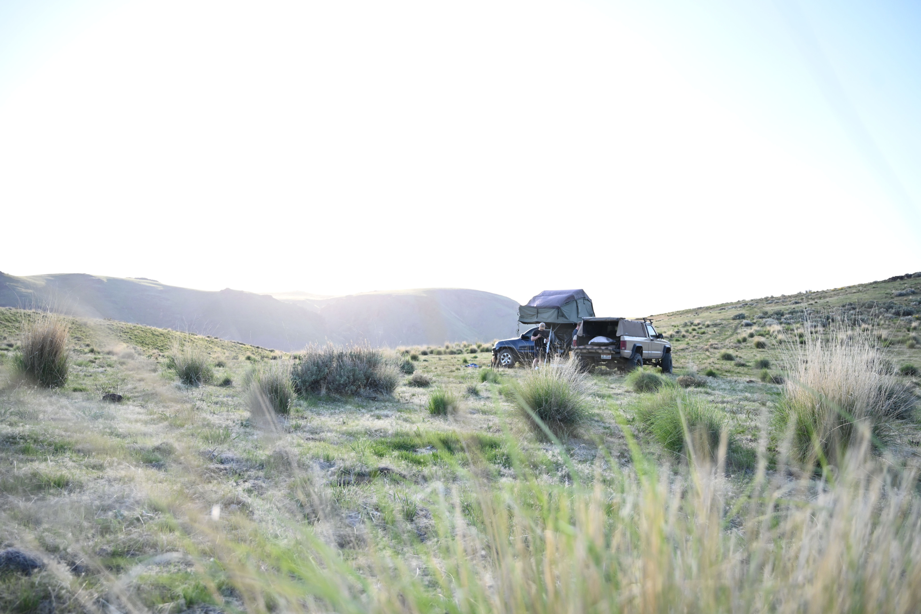 A 4x4 vehicle is set up for overland camping in a remote grassland at dusk.