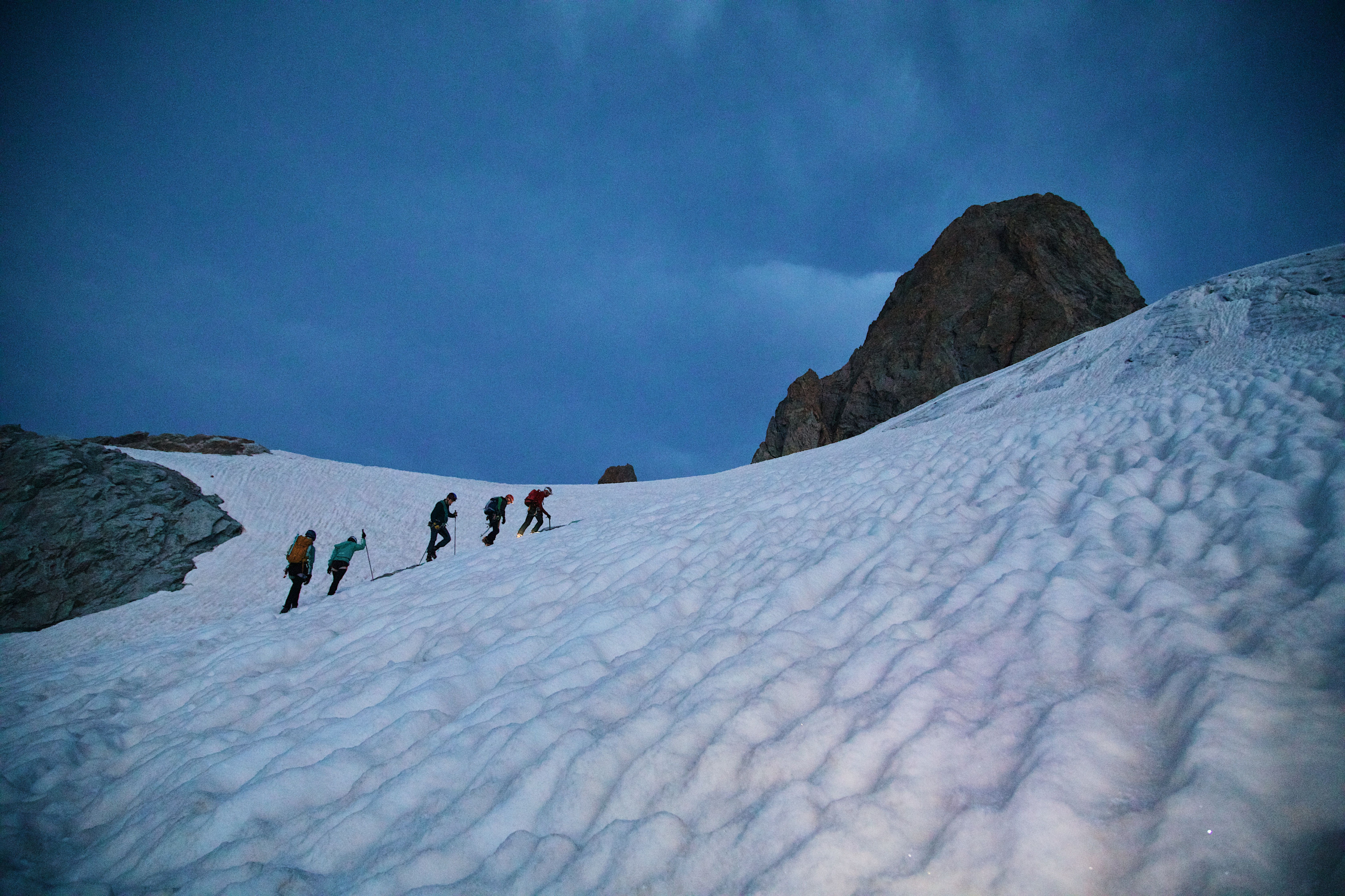 A group of climbers making their way up a snowy mountain slope at twilight.
