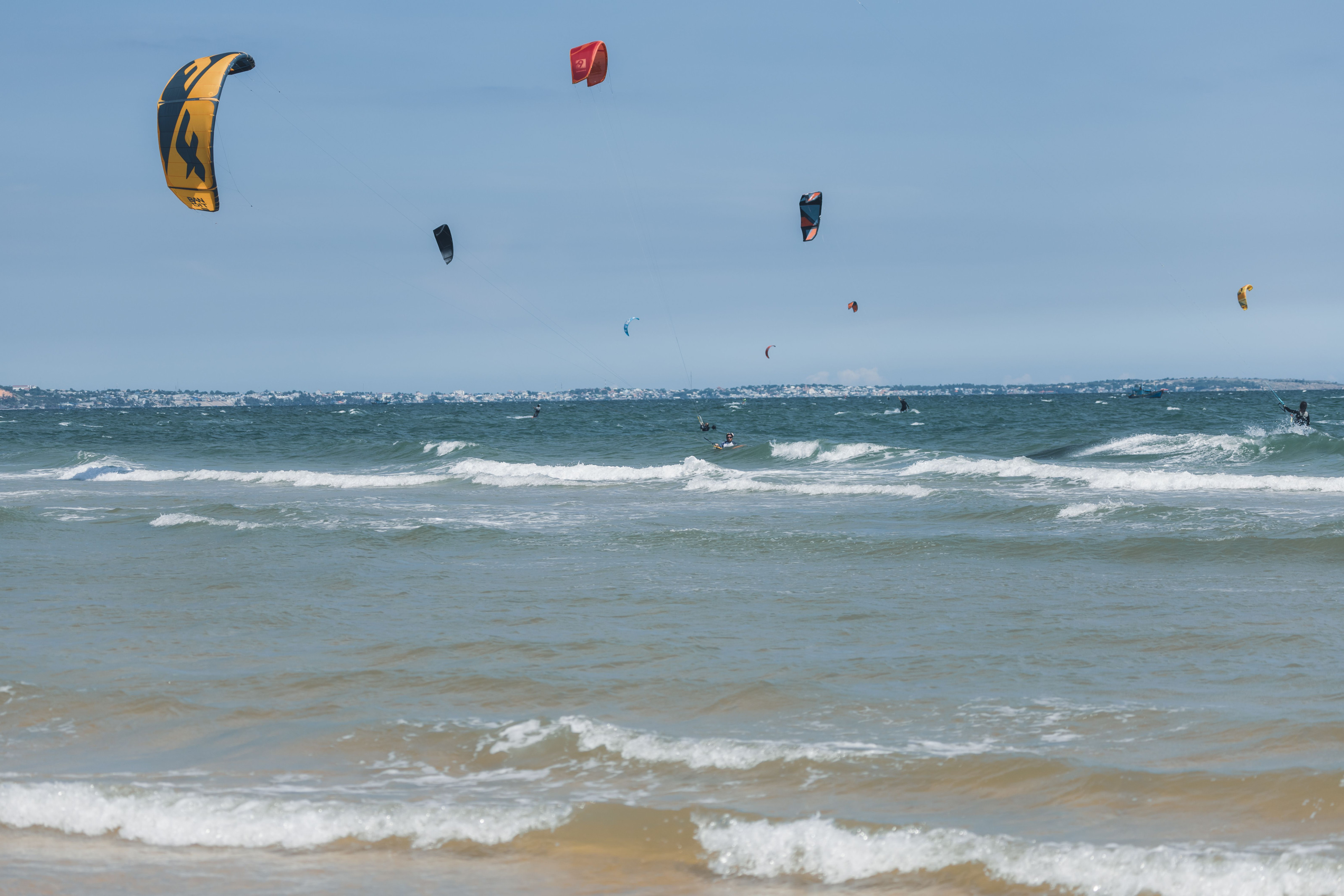Kitesurfers glide across the shallow turquoise lagoon under a bright coastal sky.