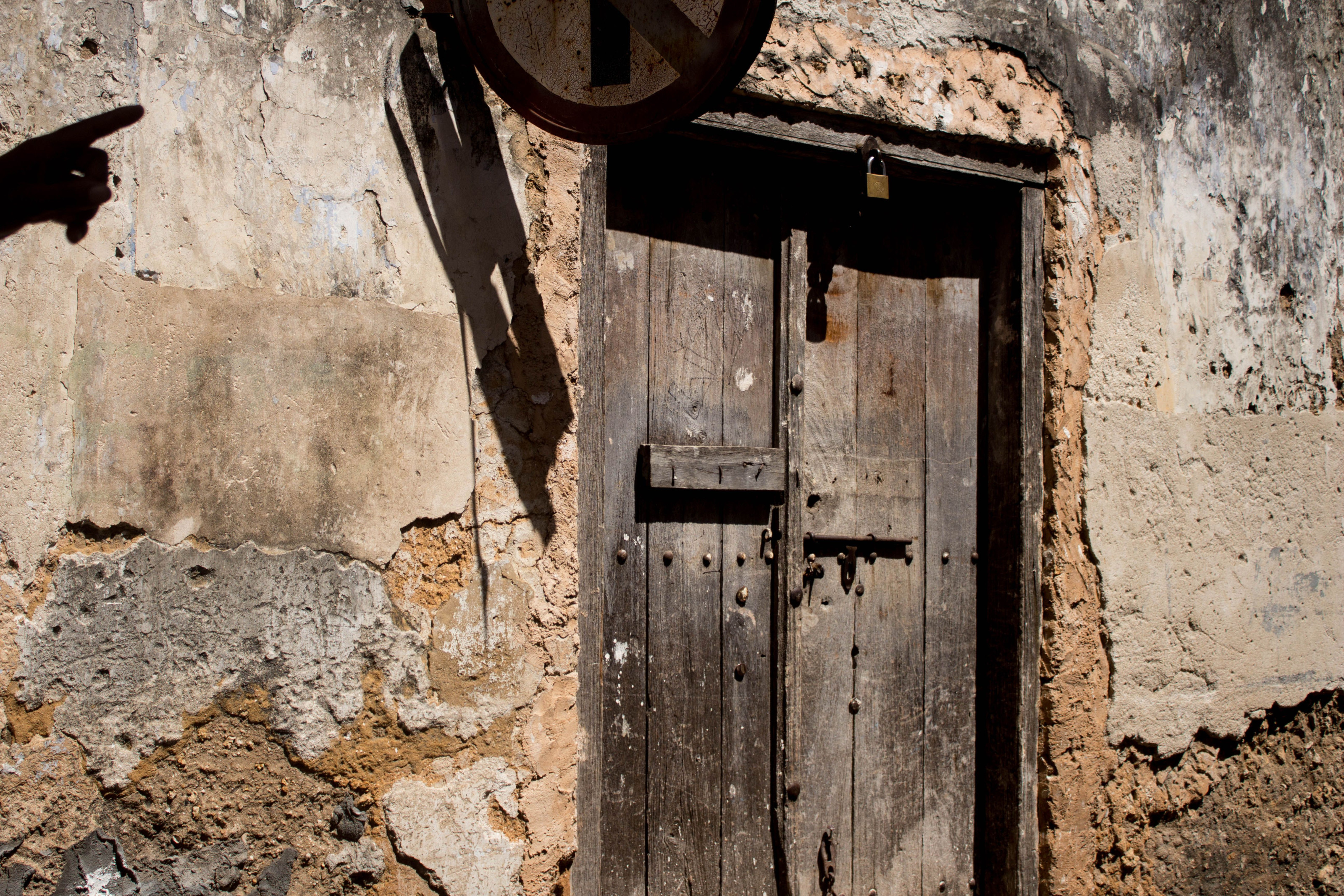 An old carved wooden door sits within a weathered stone archway in a Zanzibar alley.
