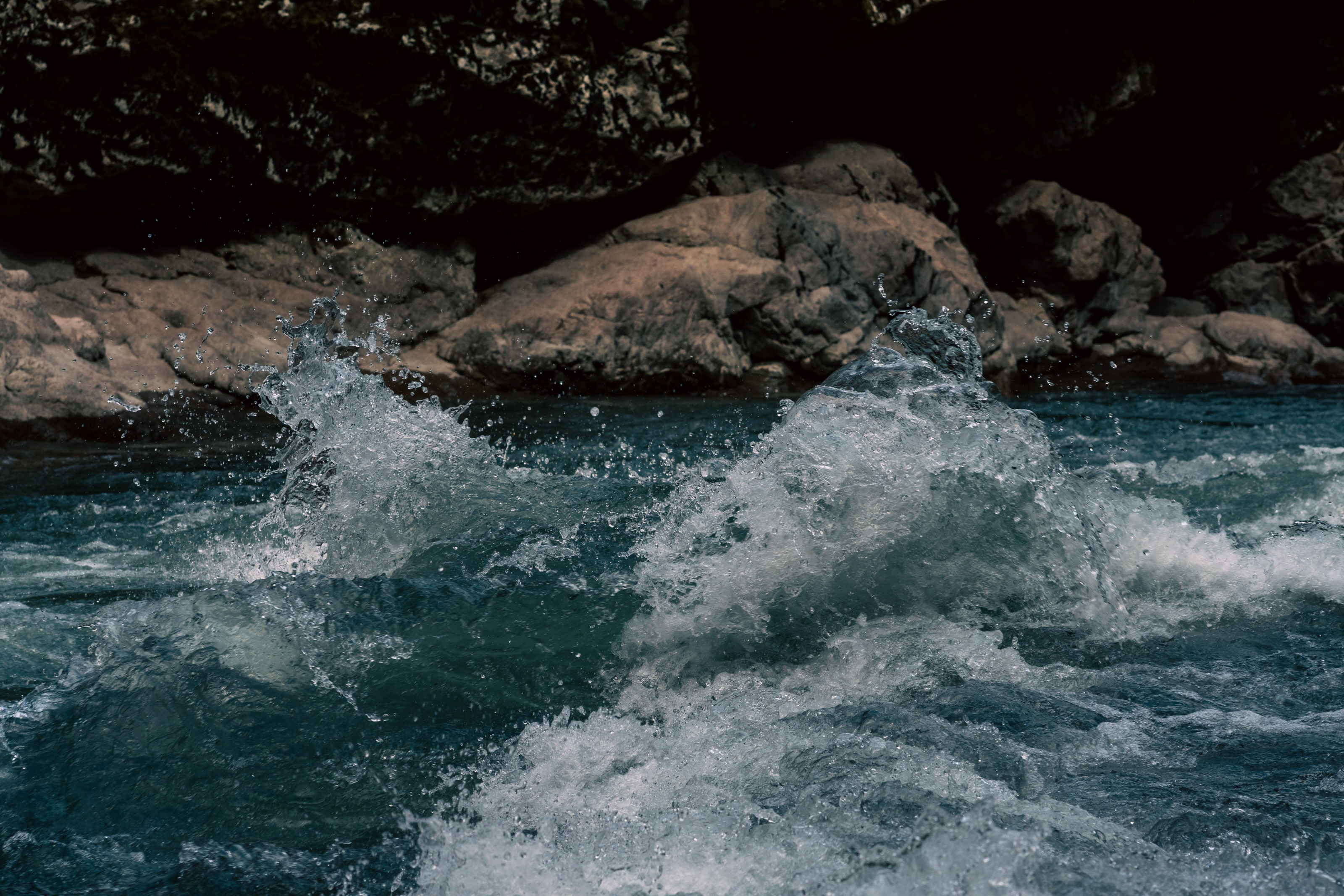 Whitewater surges and splashes against dark rocks in a river gorge.