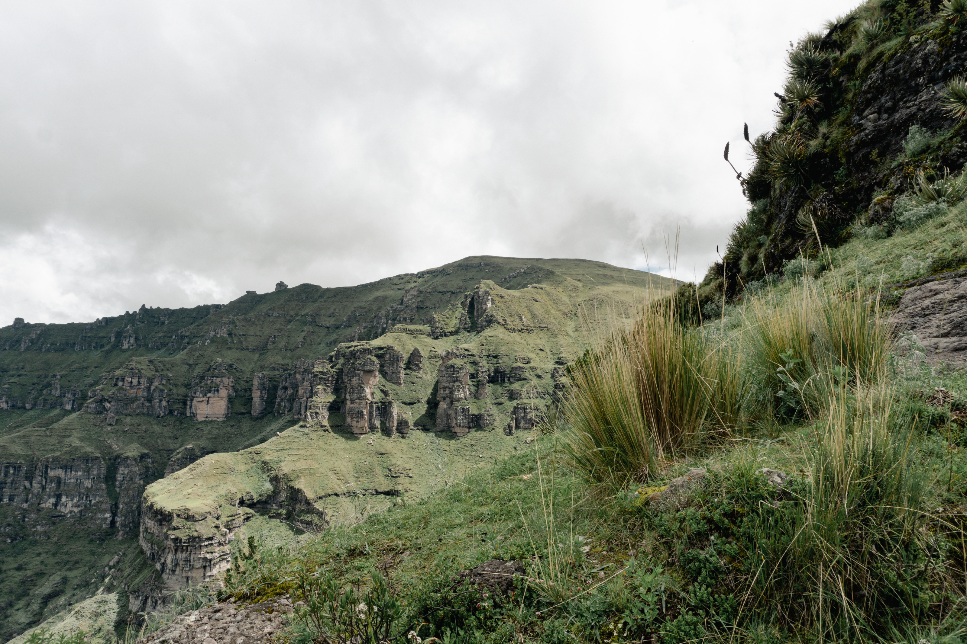Rugged green highland hills roll toward the horizon beneath a cloud-dappled sky.