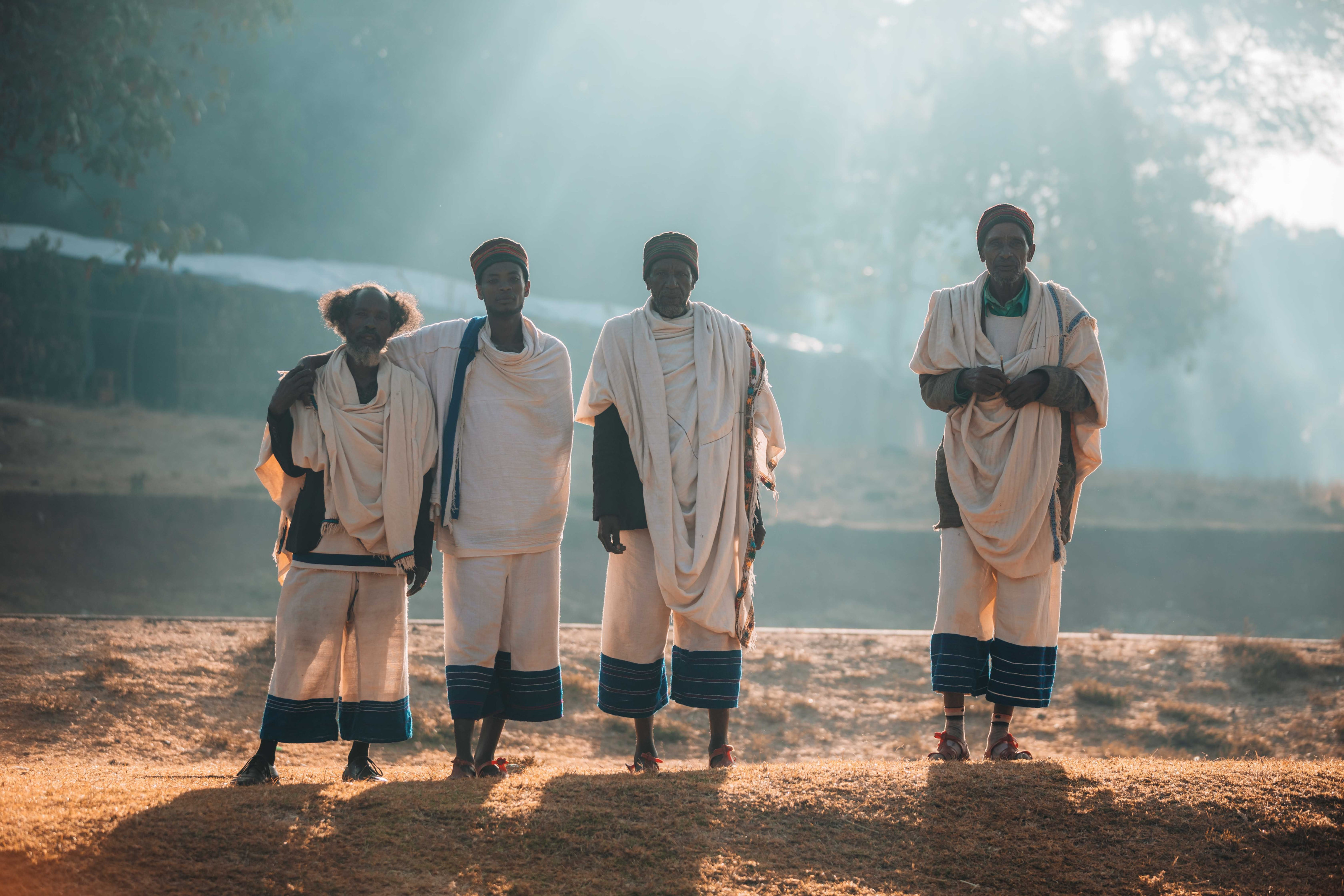 A group of people in traditional dress standing together in a rural landscape at sunrise.