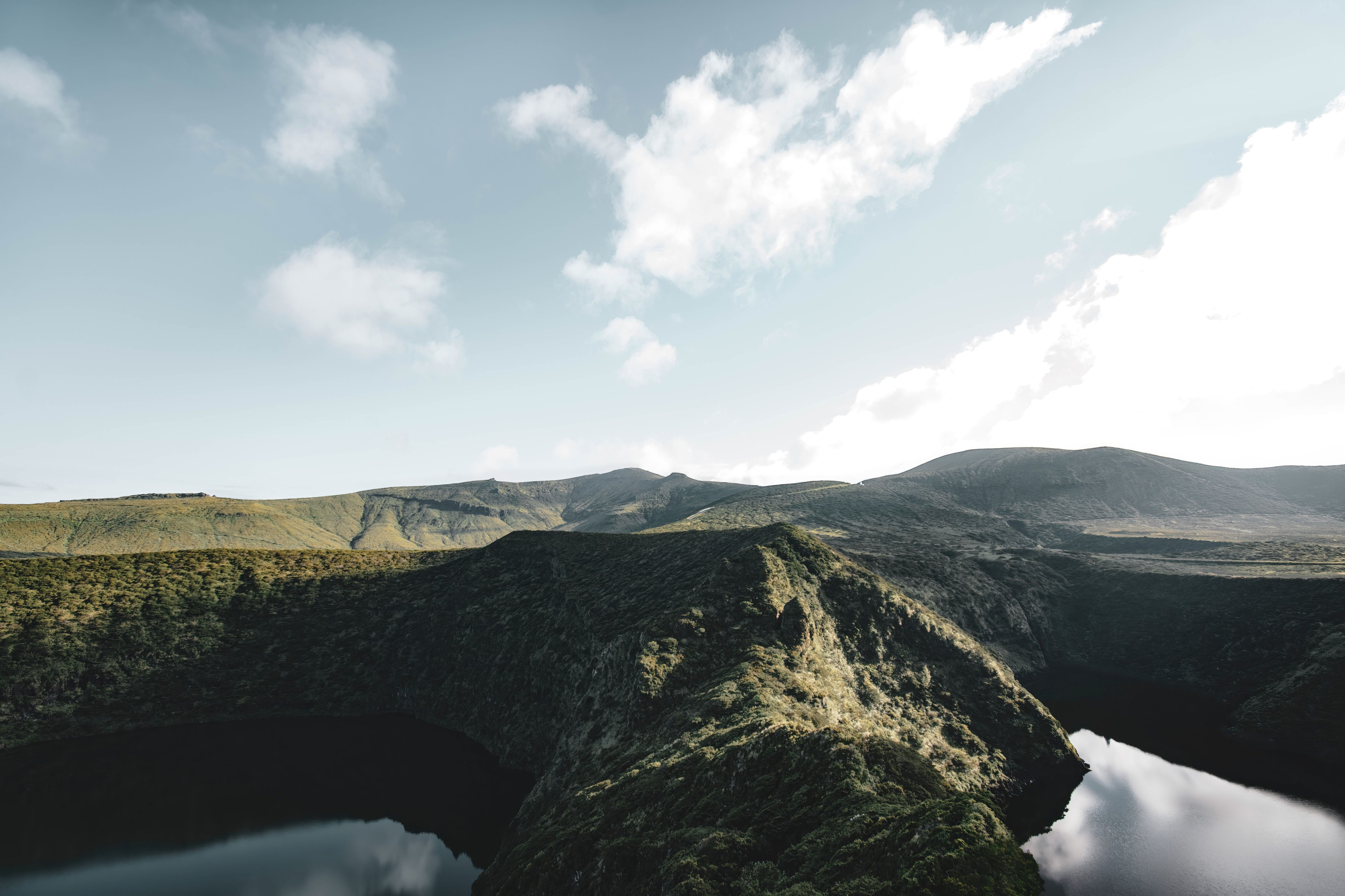 A volcanic crater lake surrounded by lush green hills under a bright sky.