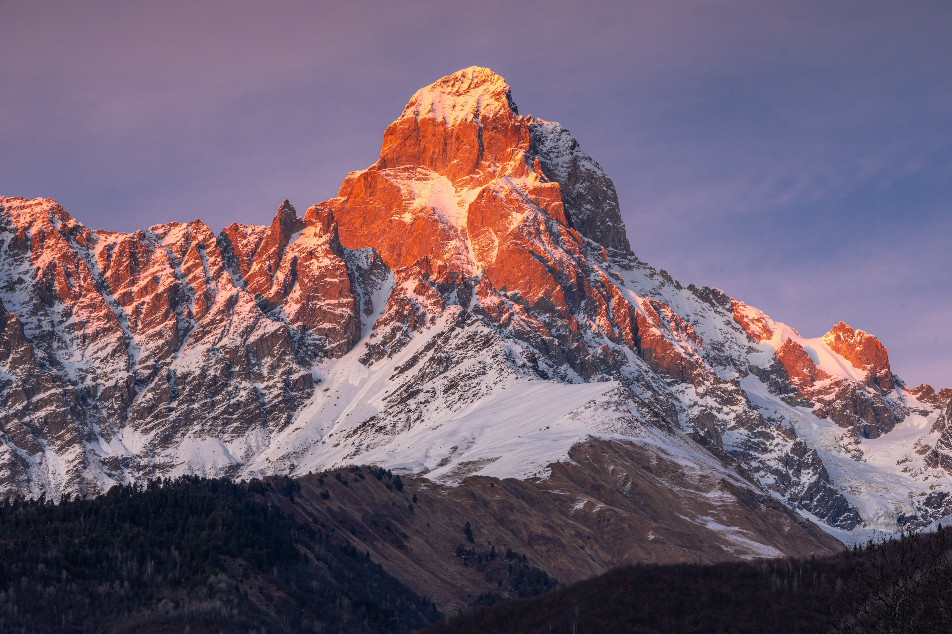 A snow-capped mountain peak glows with a reddish sunset light.