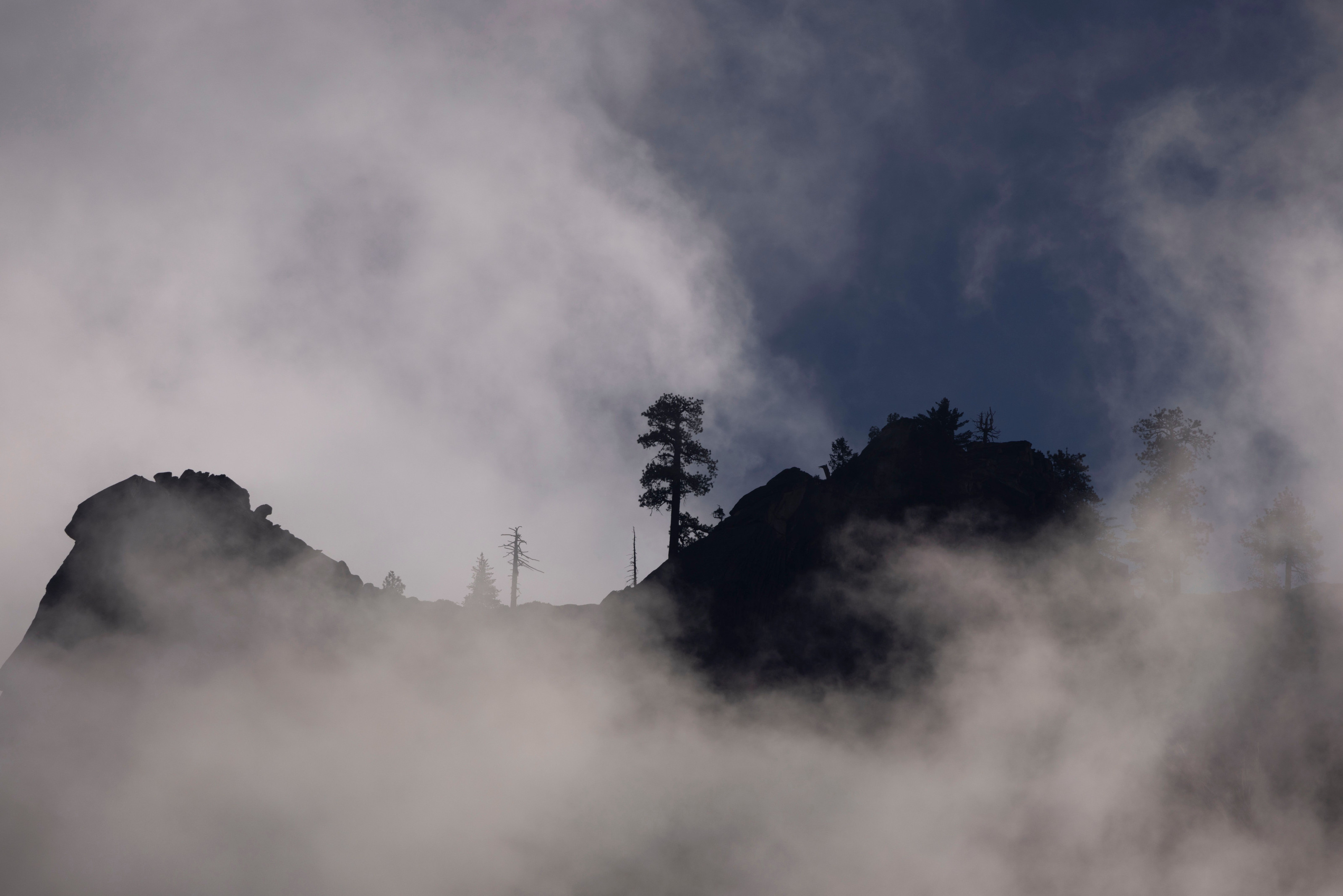Silhouetted mountain peaks rise through drifting mist above a dense forested ridge at dawn.