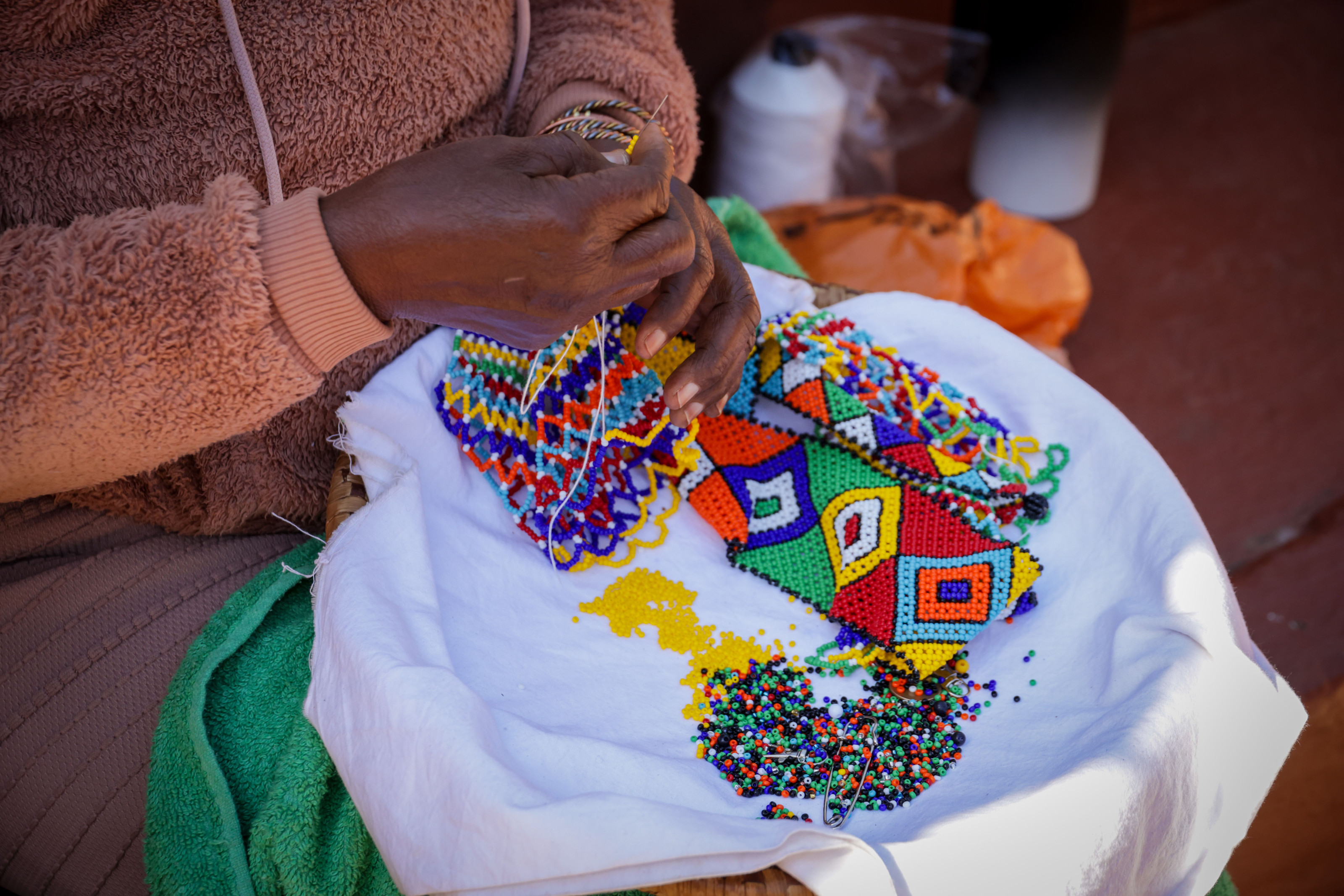A close-up of hands threading colorful beads into an intricate traditional pattern.