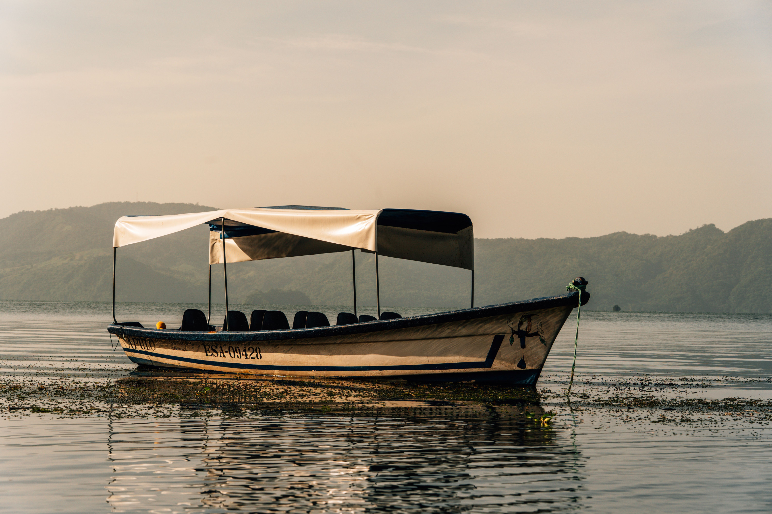 A boat resting on a calm lake with volcanic hills rising in the background at dawn.