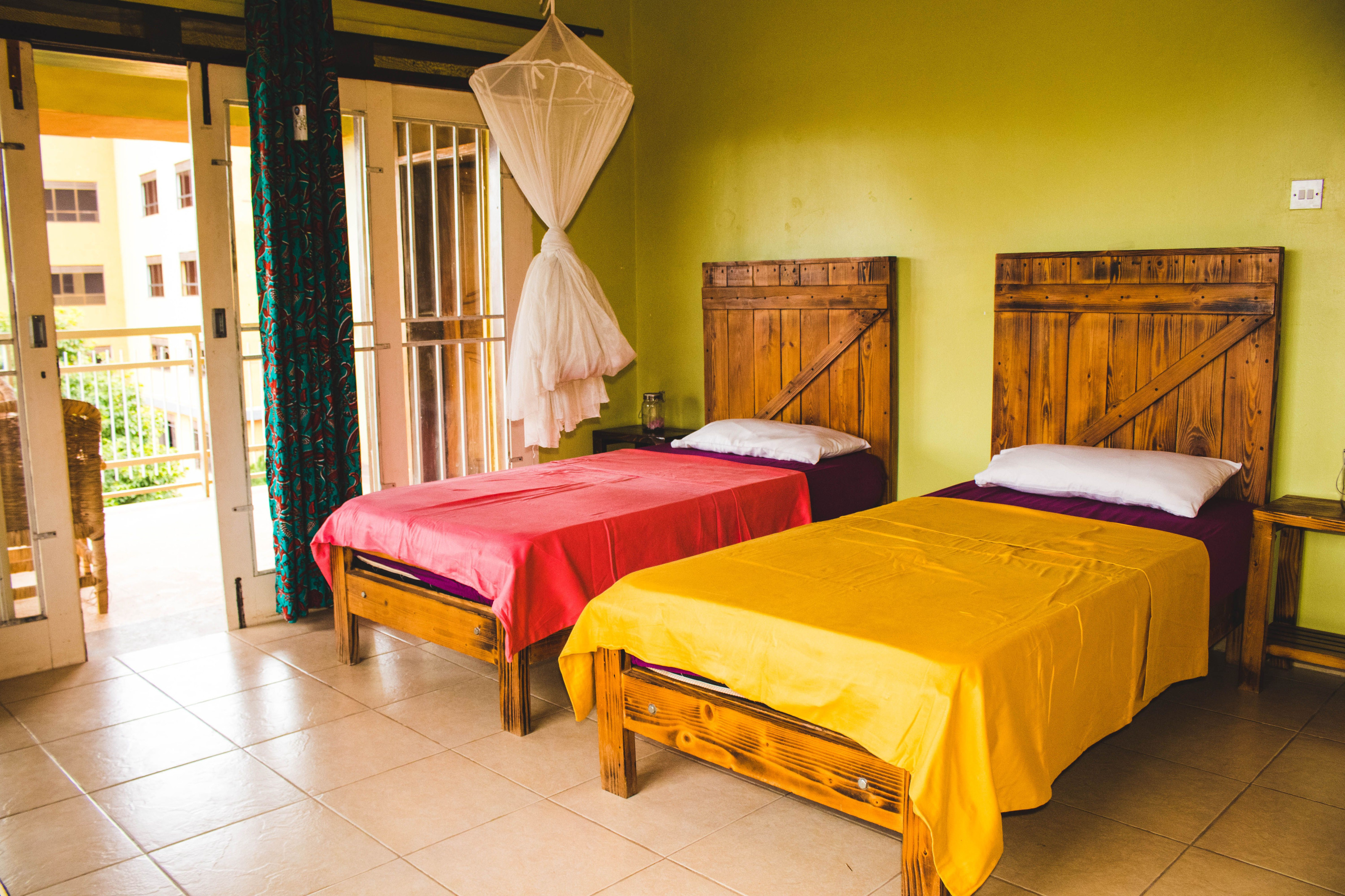 Twin beds draped in white mosquito netting inside a warmly lit lodge room in Kampala, Uganda.