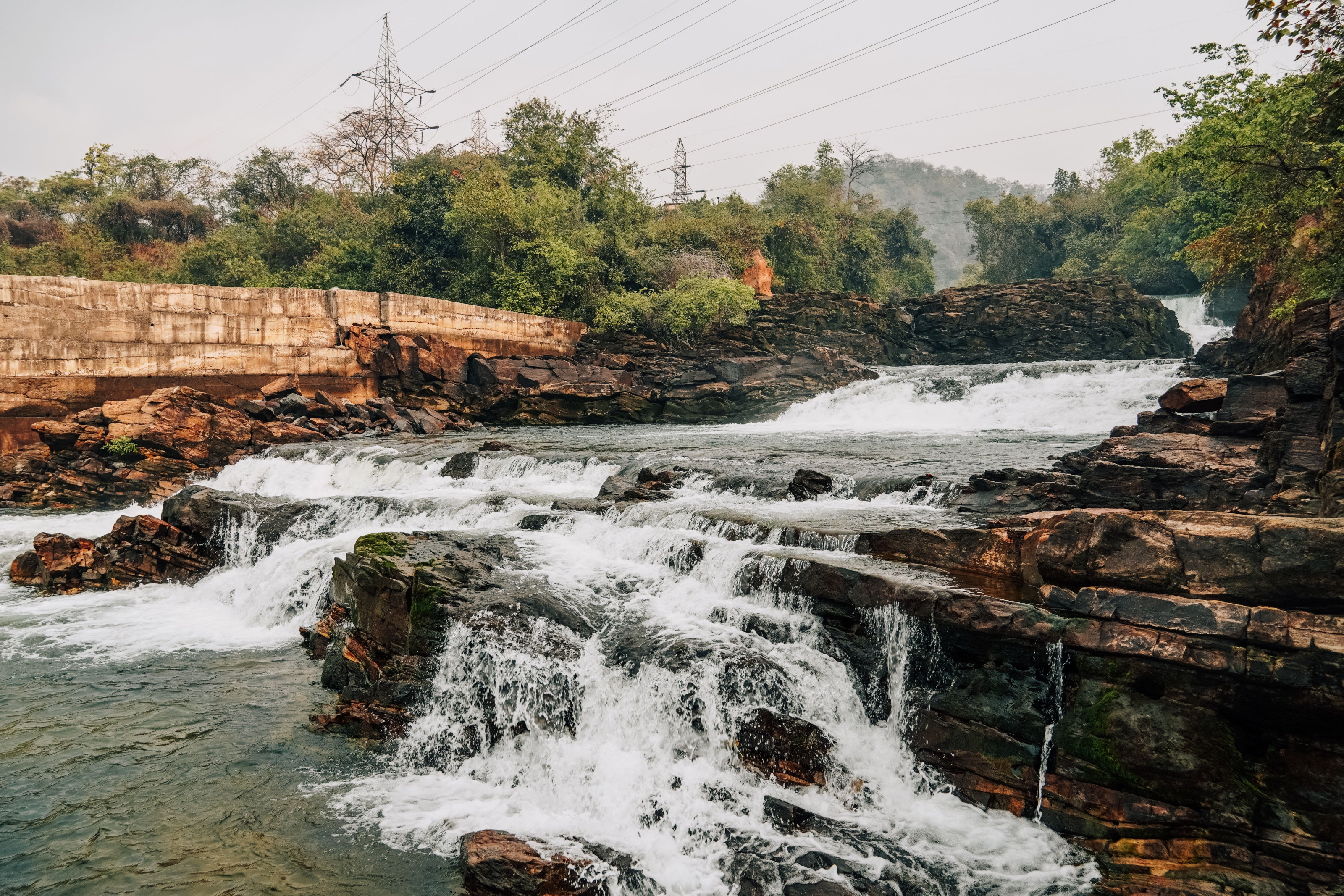 A river tumbles over rocky cascades between banks of lush green vegetation.