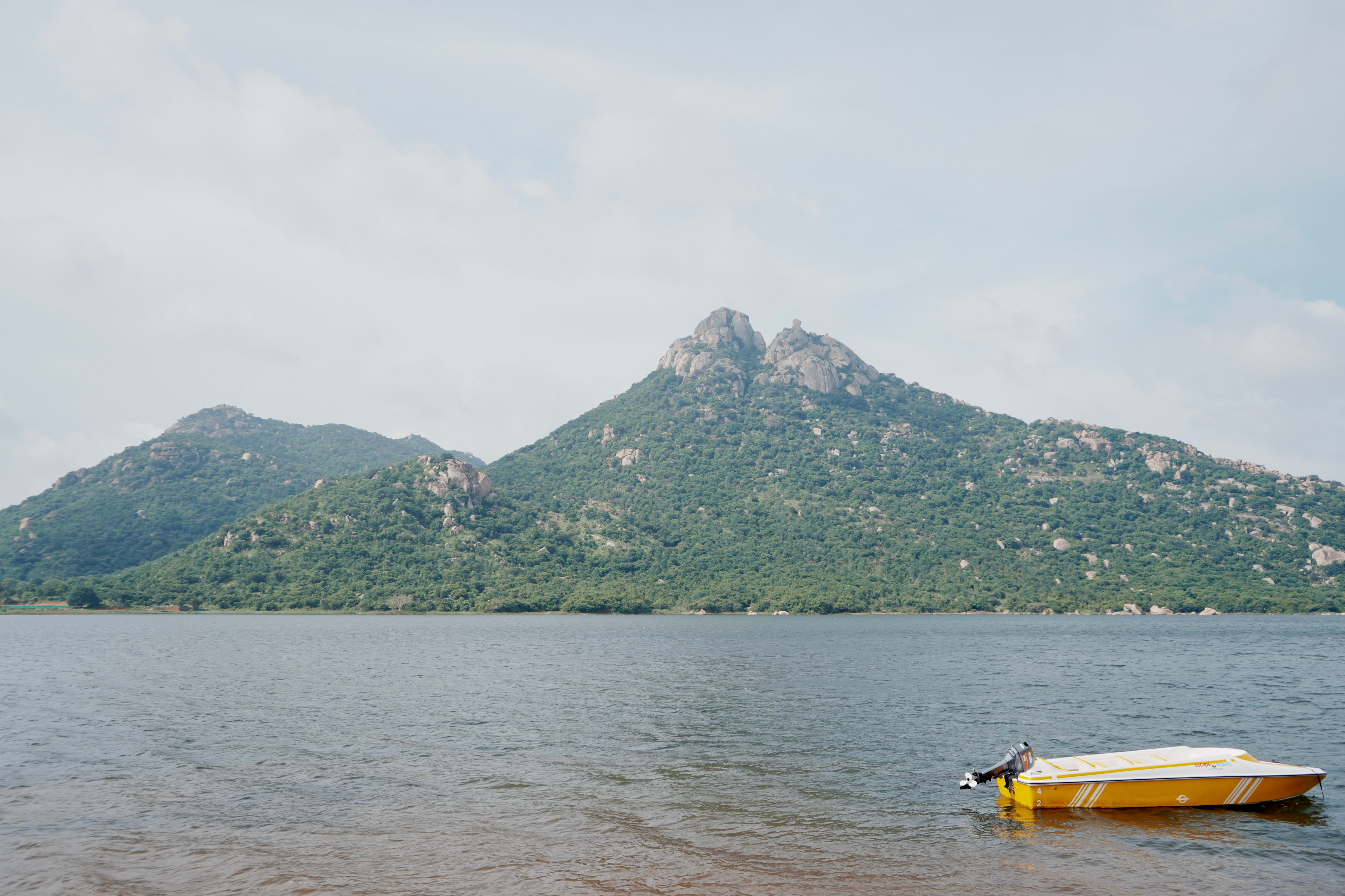 A small yellow boat drifts on a calm lake framed by forested mountain slopes.