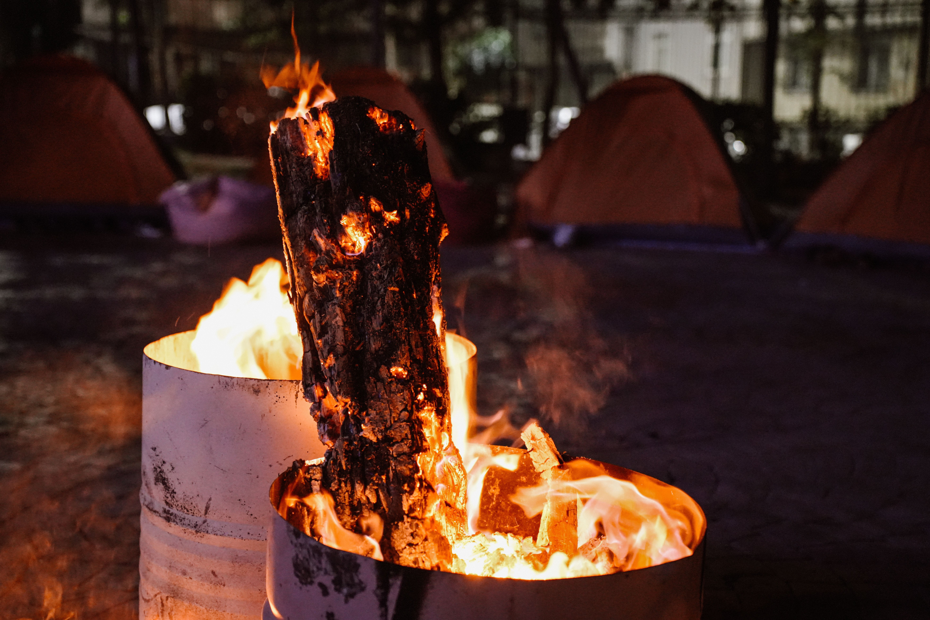 A glowing campfire burns at dusk in front of safari tents at a bush camp.