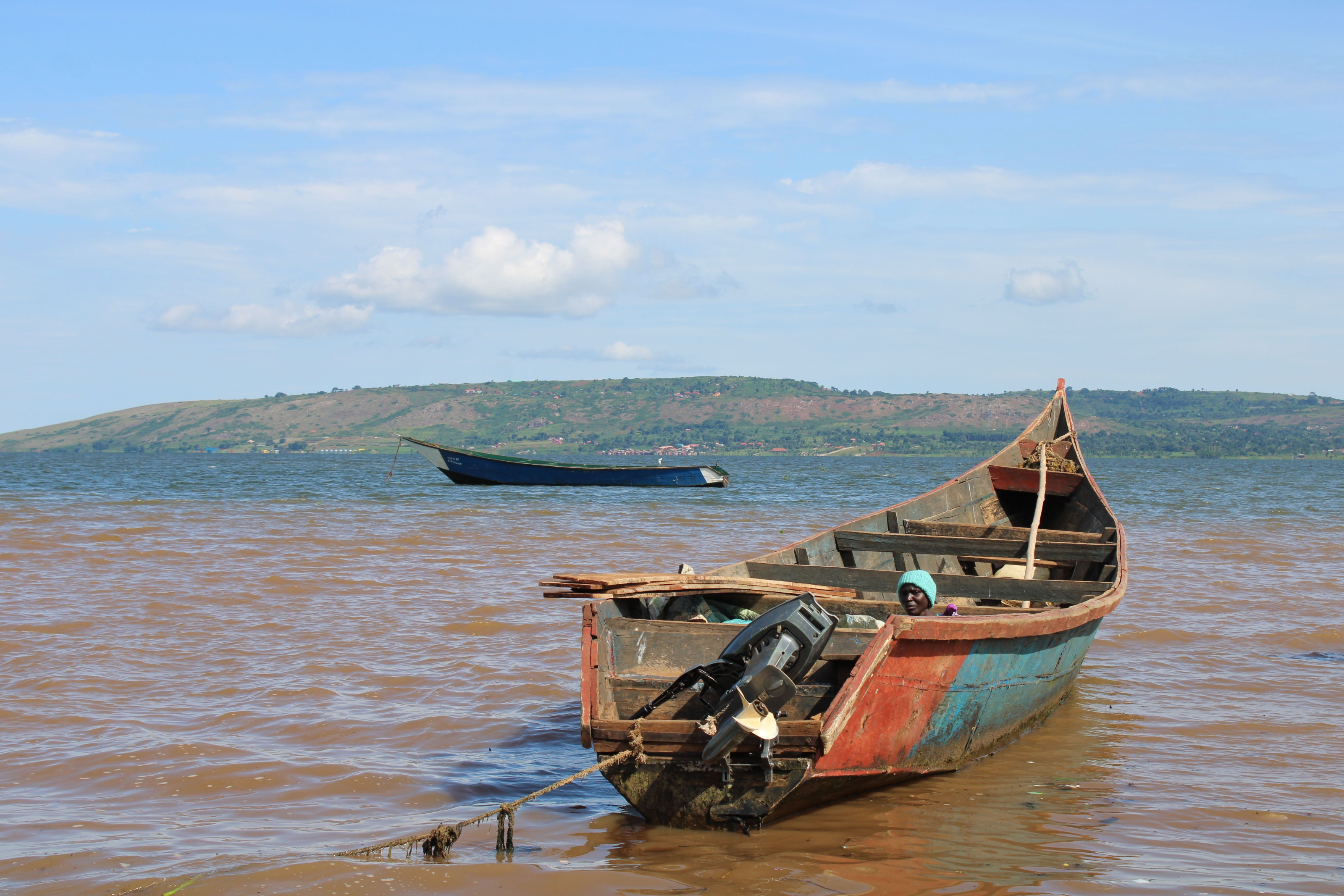 A rustic wooden fishing boat rests moored at the edge of a calm Ugandan lake.