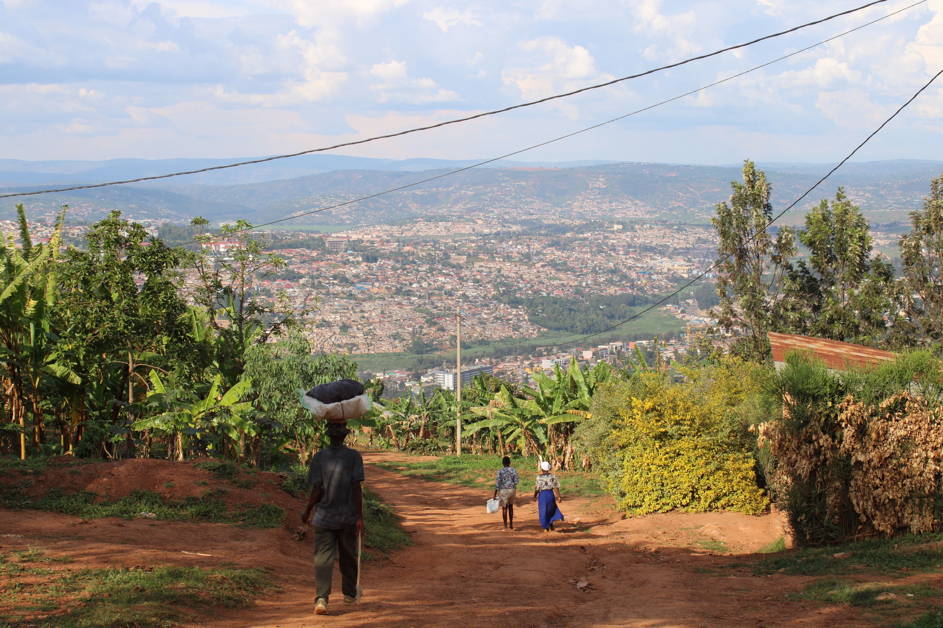 People walk along a rural path overlooking Kigali's hillside sprawl.