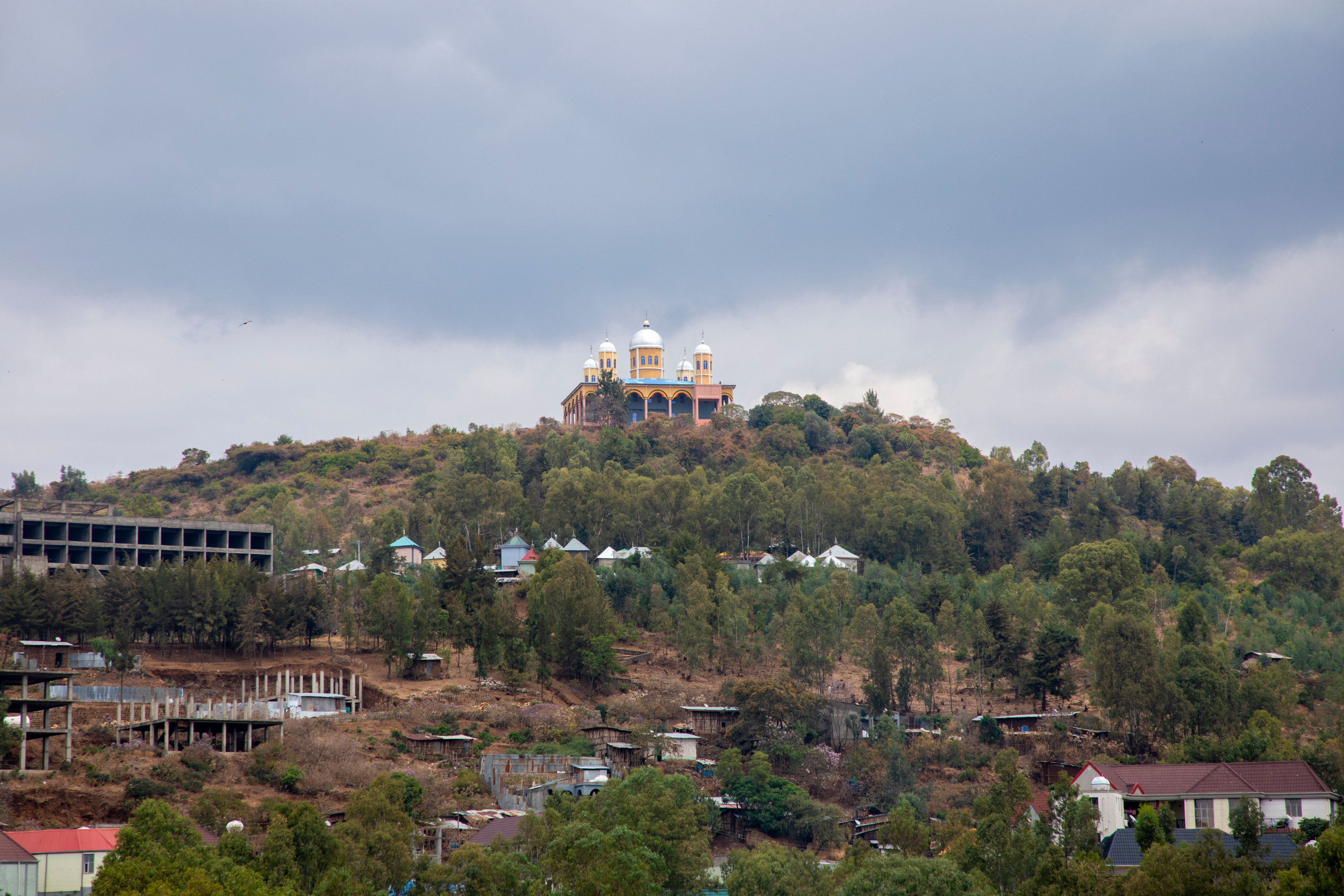 Historic stone buildings crown a green hillside beneath a cloudy Ethiopian sky.
