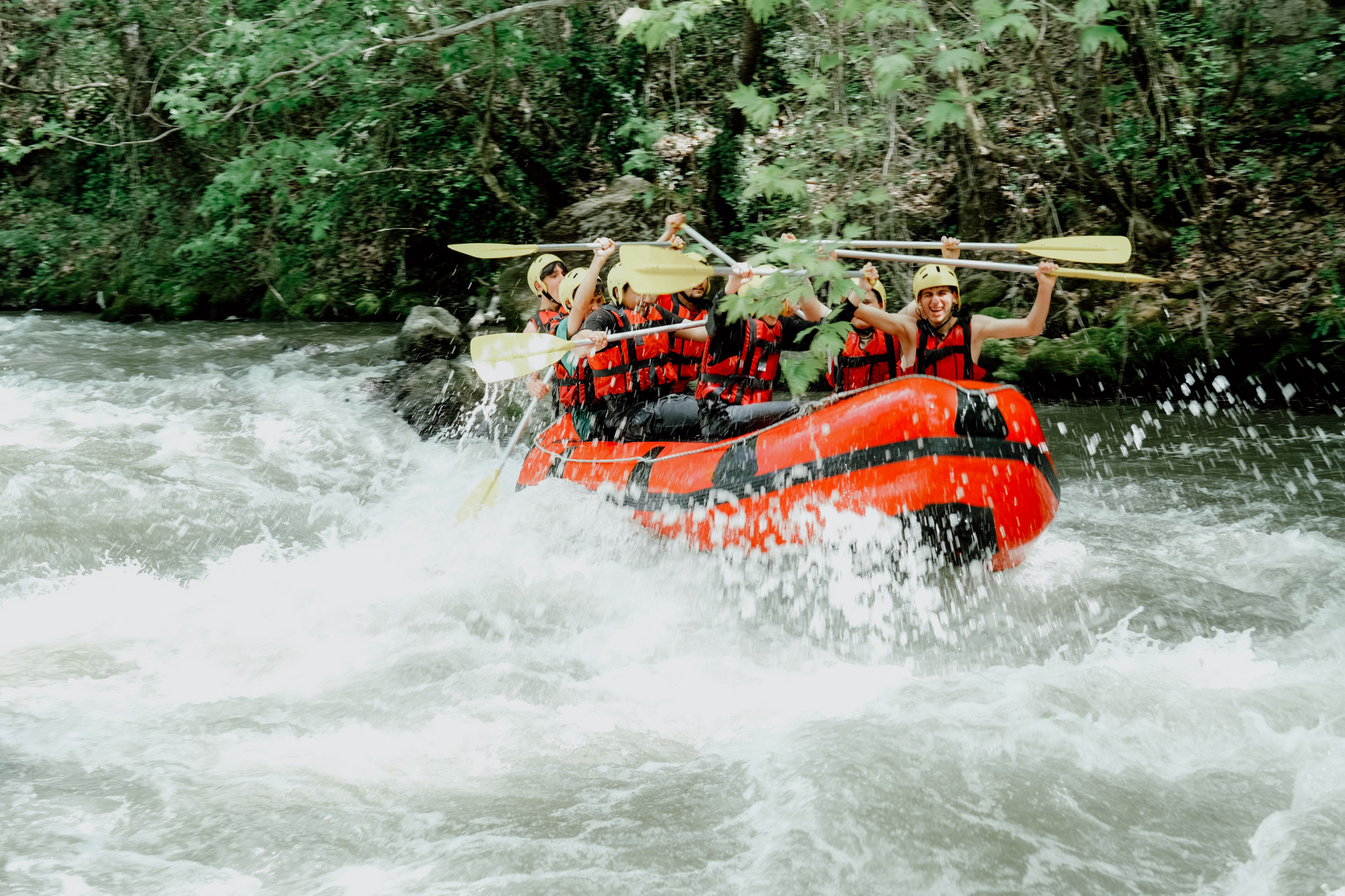 A group riding a raft is drenched in spray while crashing through river rapids.