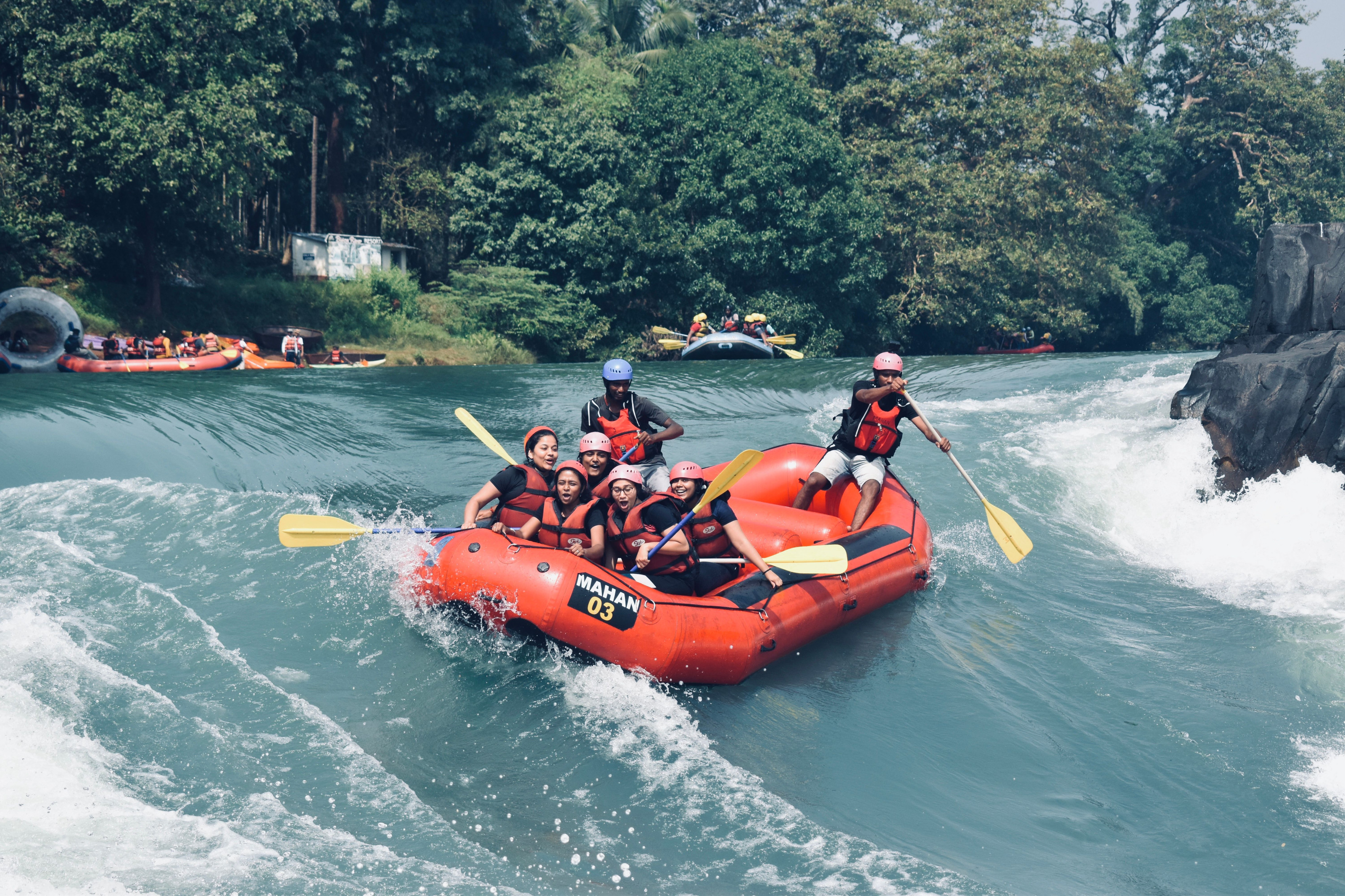 A raft crew paddles hard through churning white rapids on a wide river.