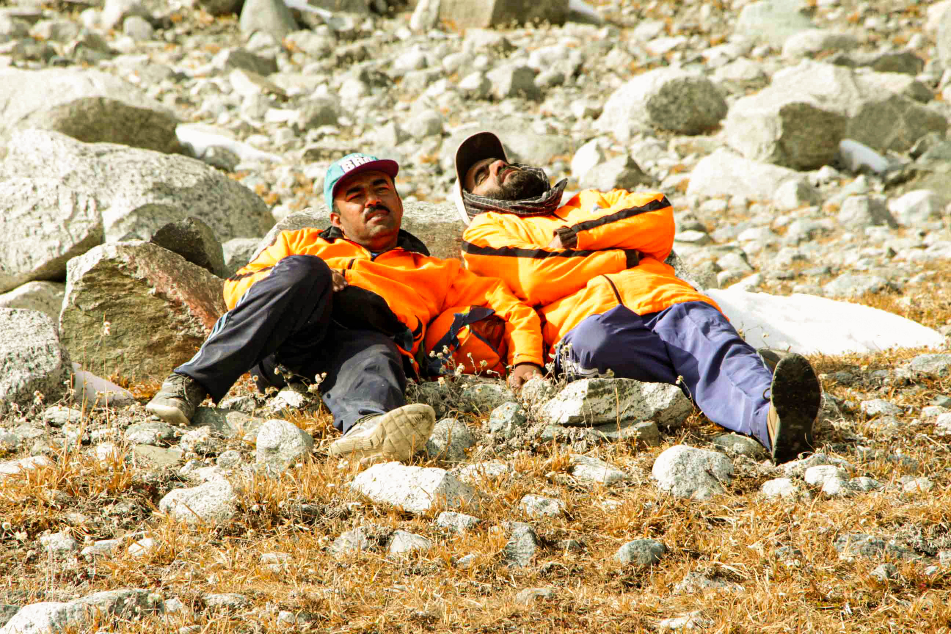 Two trekkers resting on rugged highland terrain during a mountain trek.