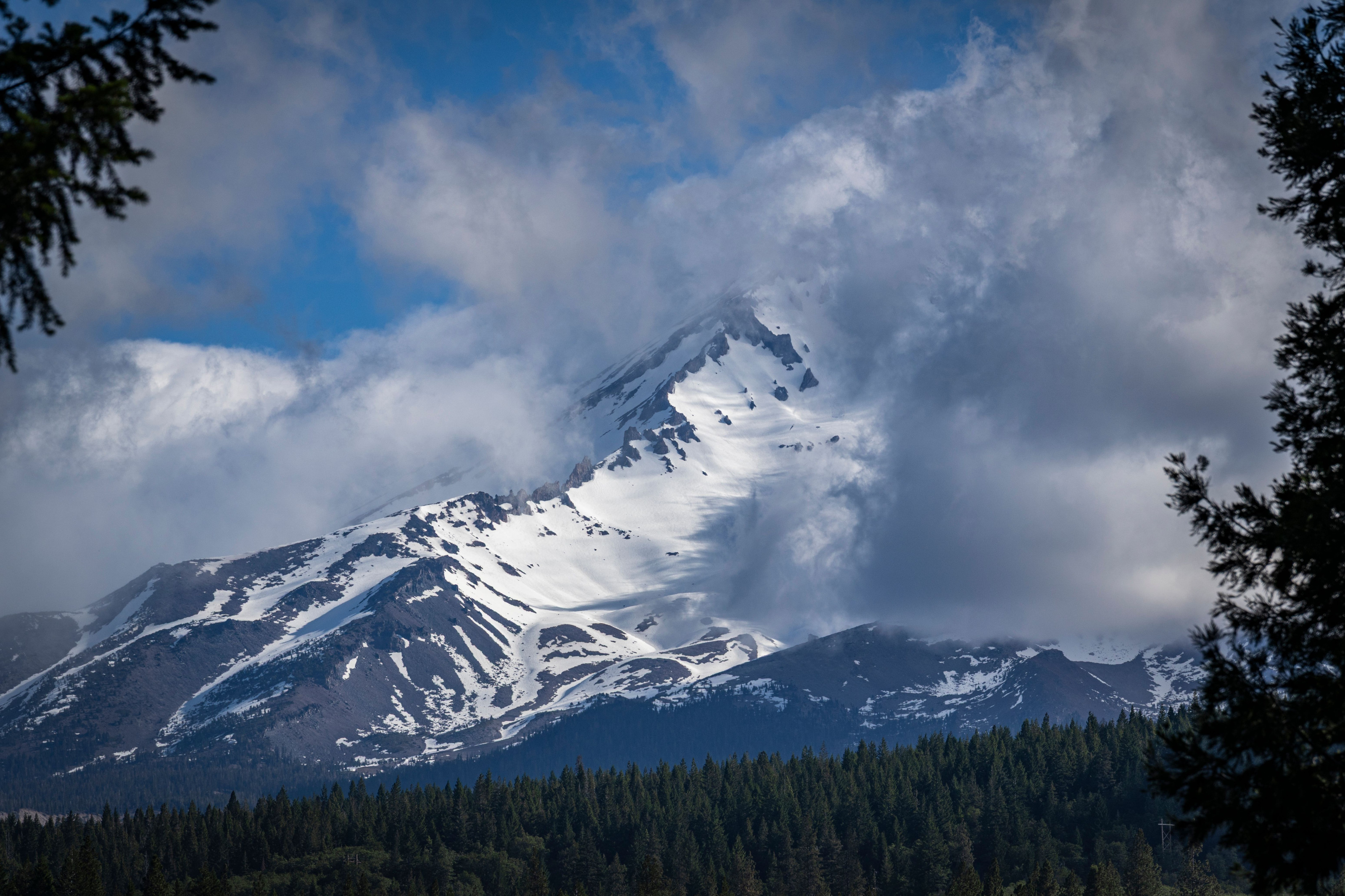 A snow-capped mountain peak rises above forested slopes, partially wrapped in cloud.