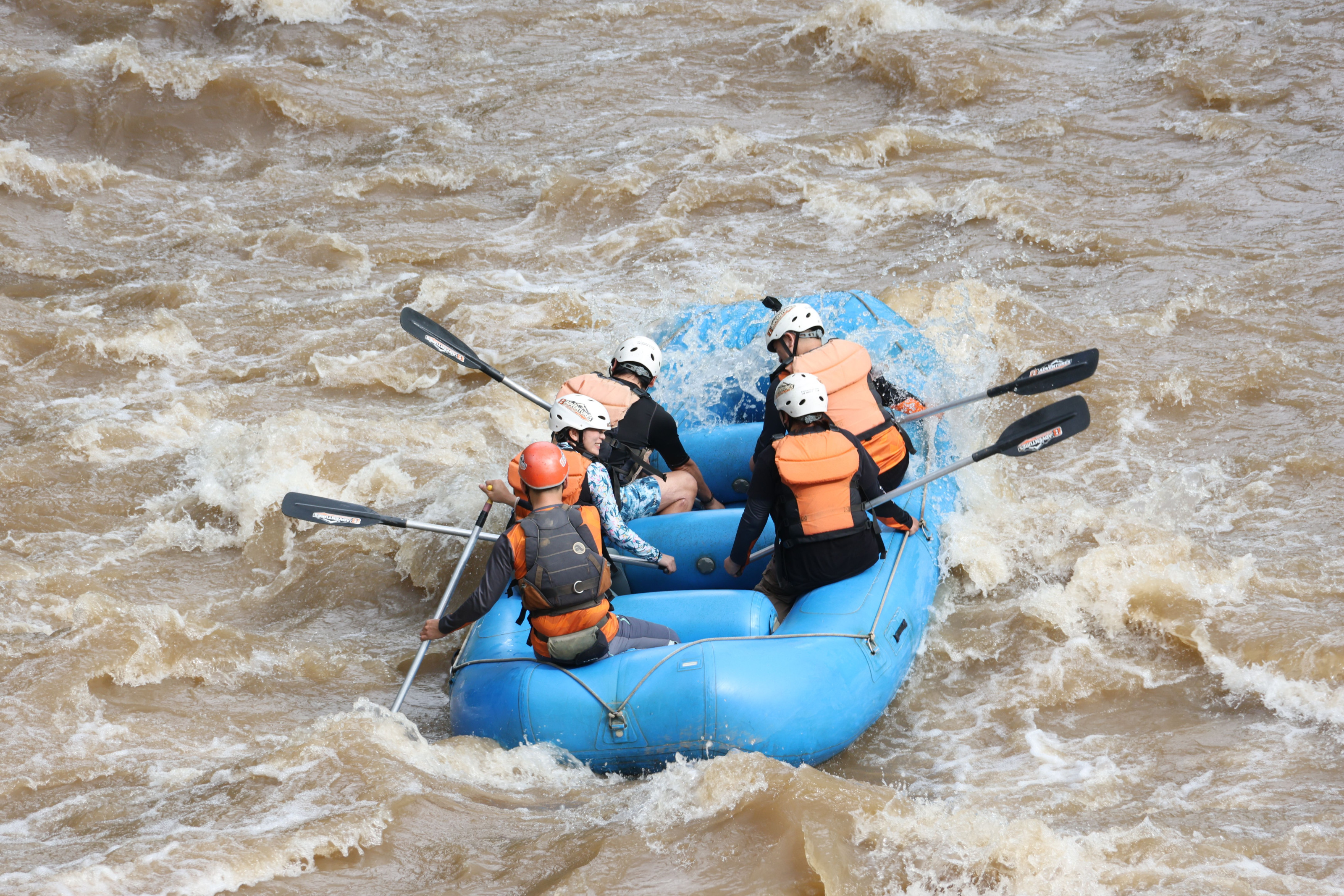 A rafting team paddles hard through churning white-water rapids in an inflatable raft.
