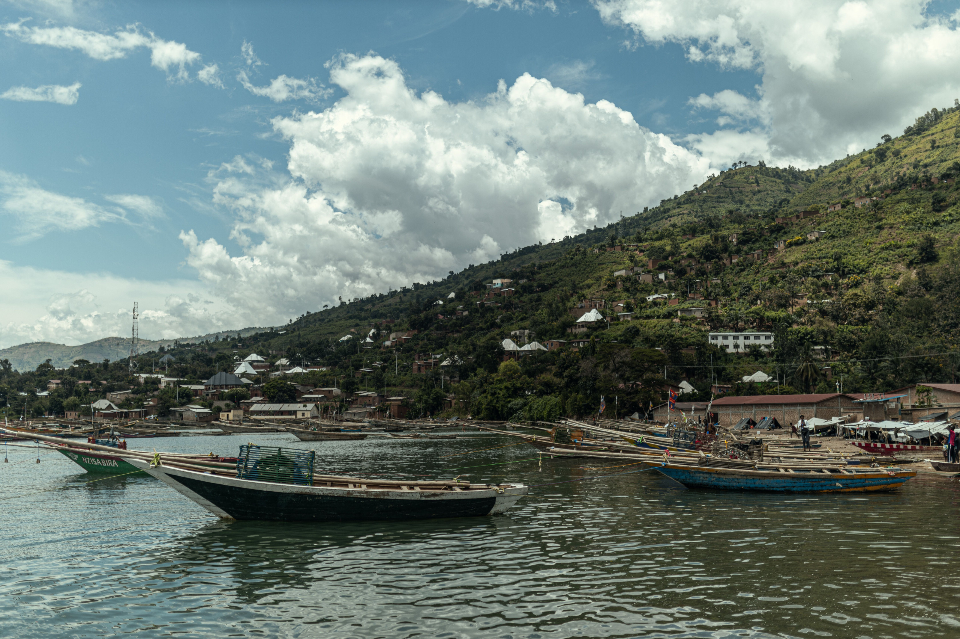 Wooden fishing boats rest on the shore of a great lake beneath forested hills.