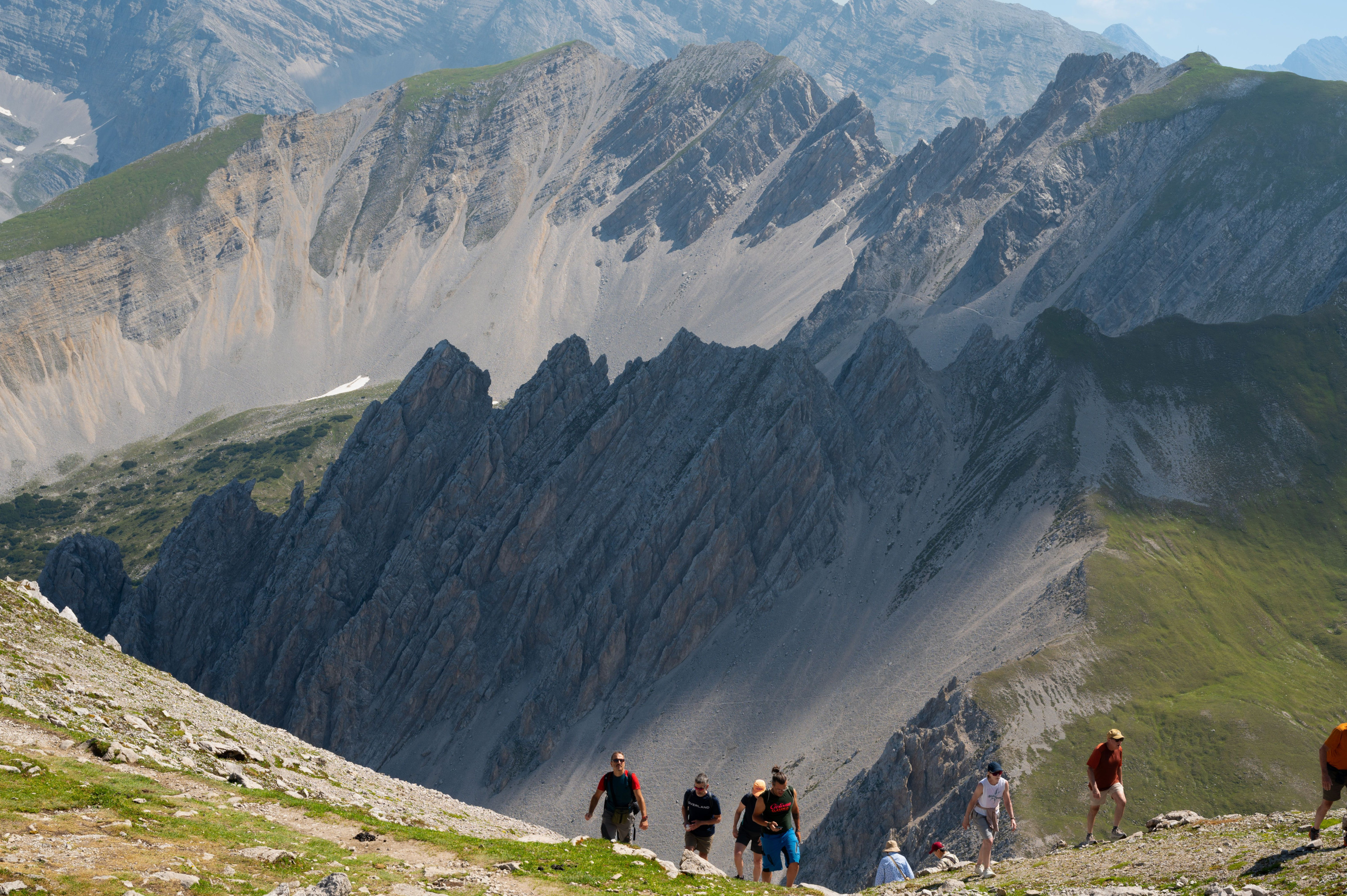 A group of hikers climbs a steep mountain ridge beneath a clear sky.