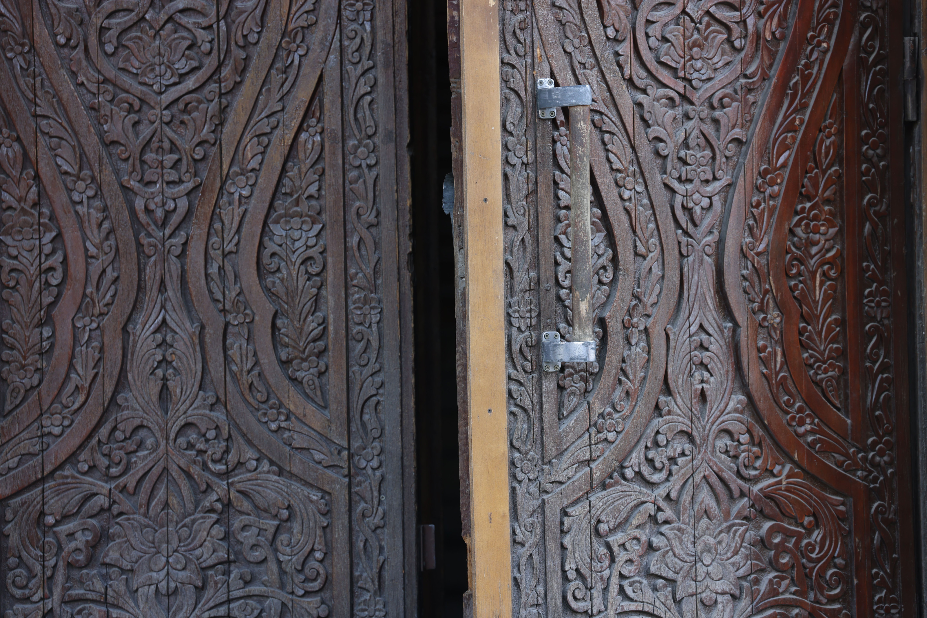 An ornately hand-carved wooden door set into a weathered stone building along a narrow alley.