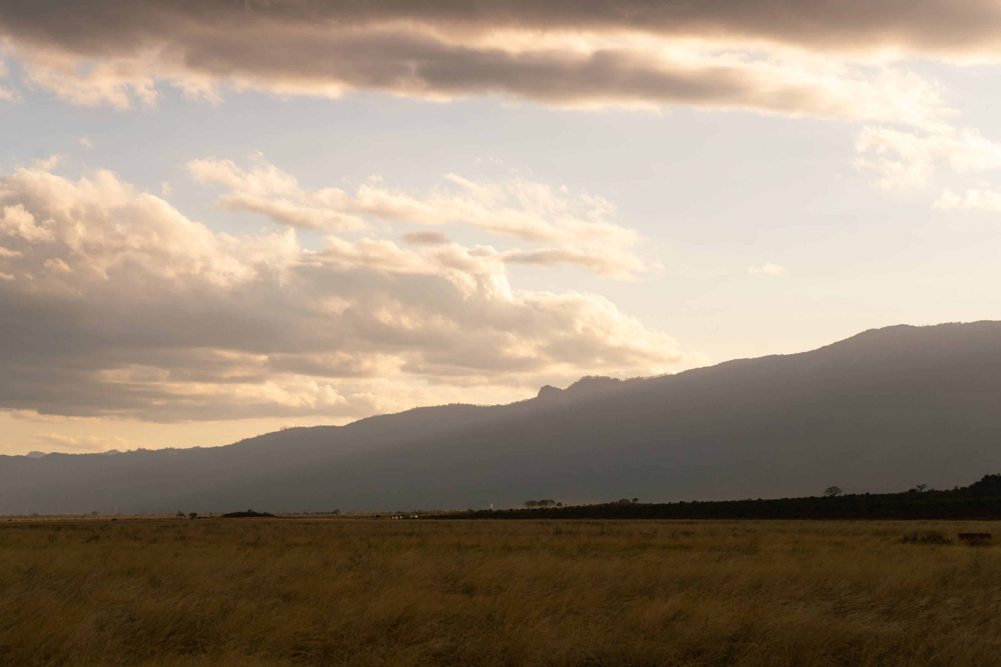 Layered hills and distant peaks stretch across the Kenyan landscape under a soft evening sky.
