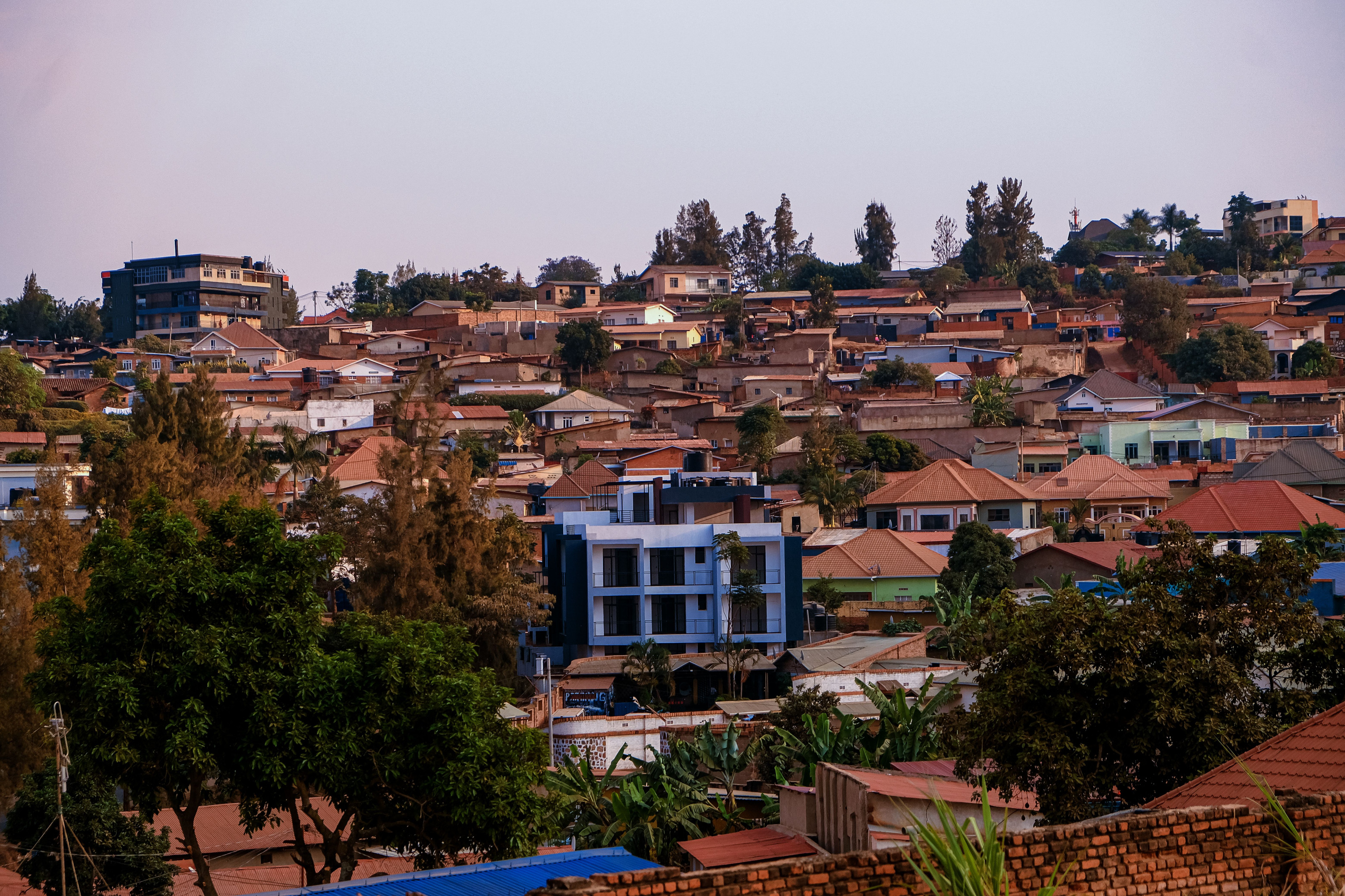 A hillside city glows warmly at sunset, its rooftops and streets nestled among green hills.