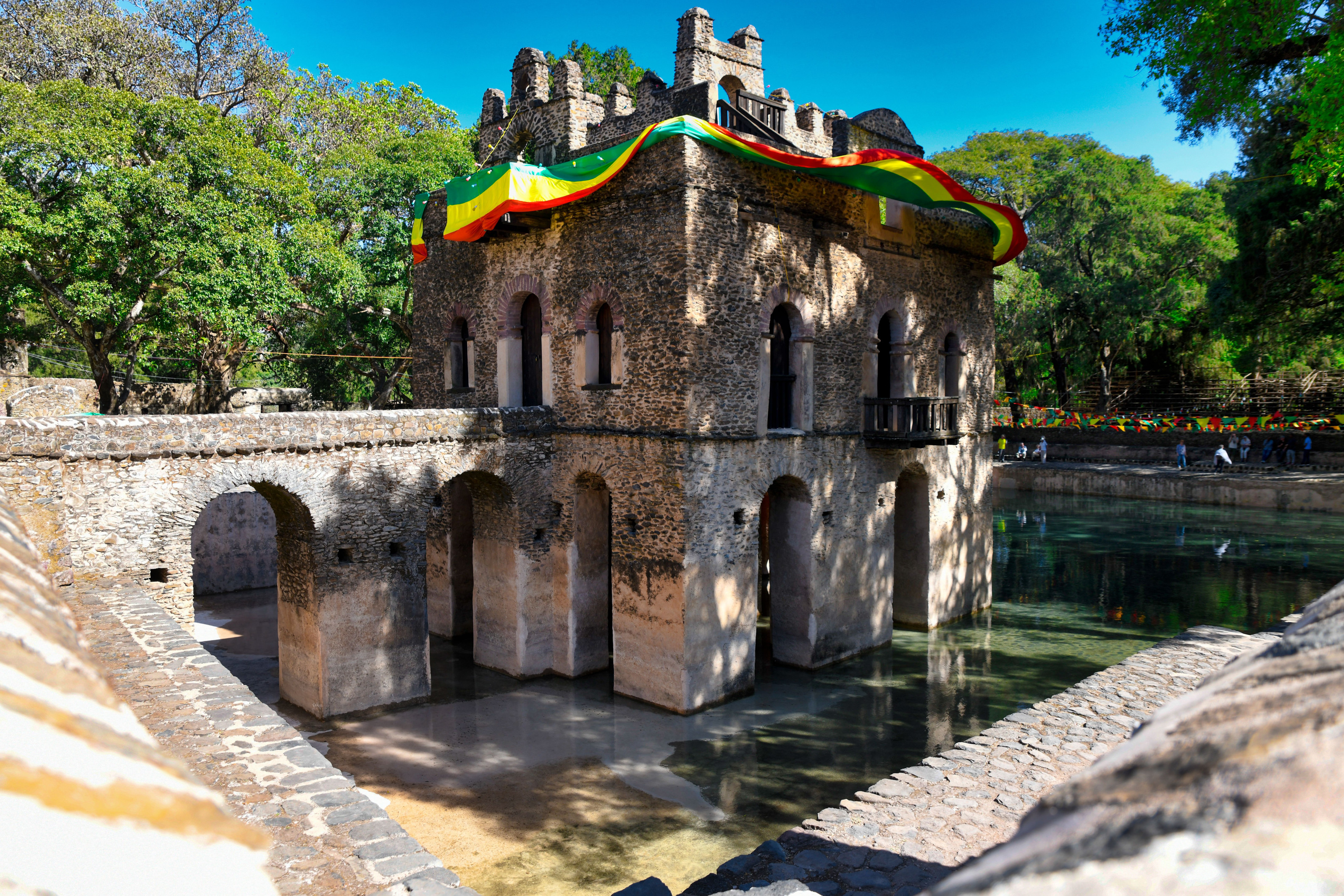 A stone bathing pavilion with arched openings stands amid lush greenery at a historic Ethiopian site.