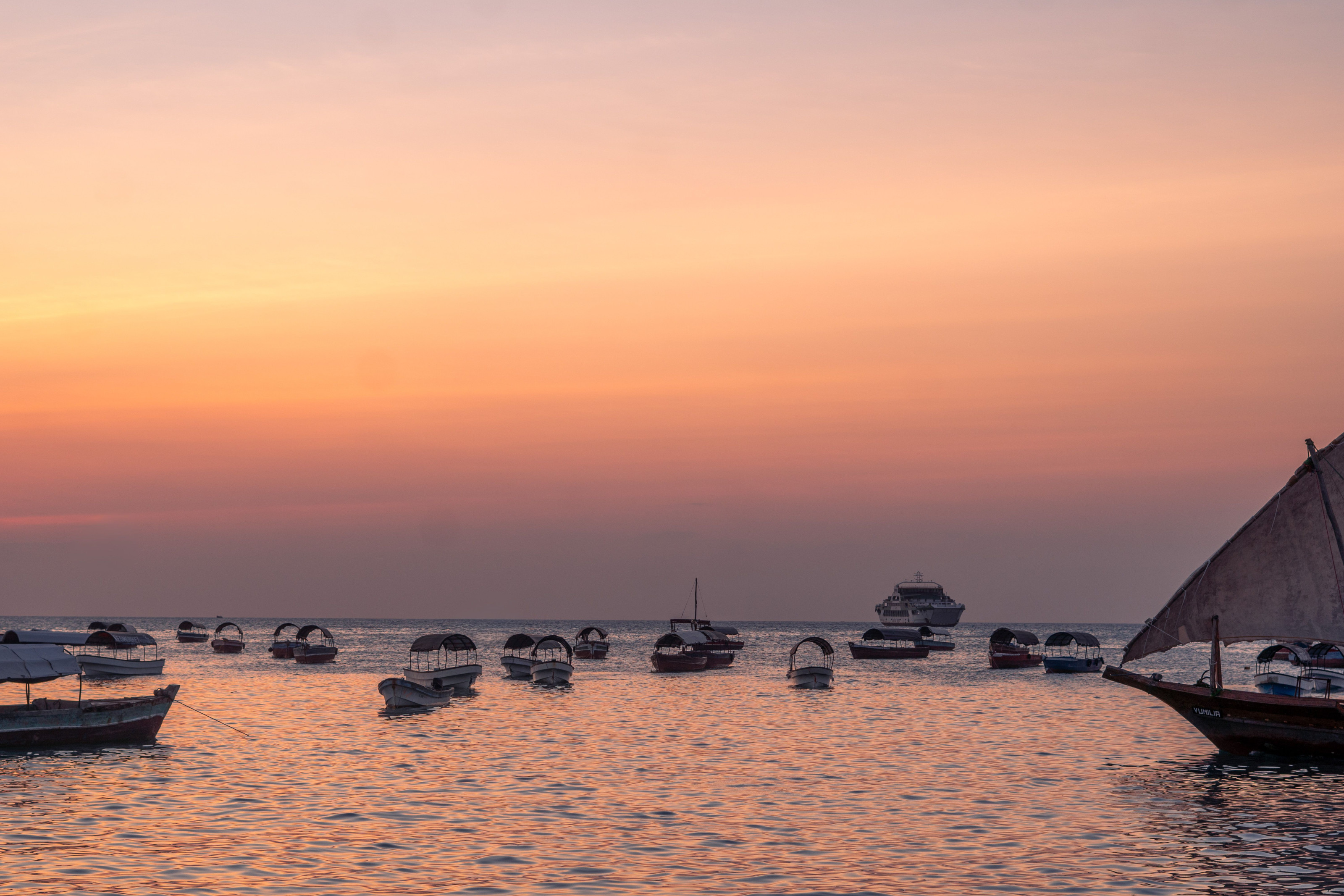 Silhouetted boats rest on still water as the sky glows orange at sunset.