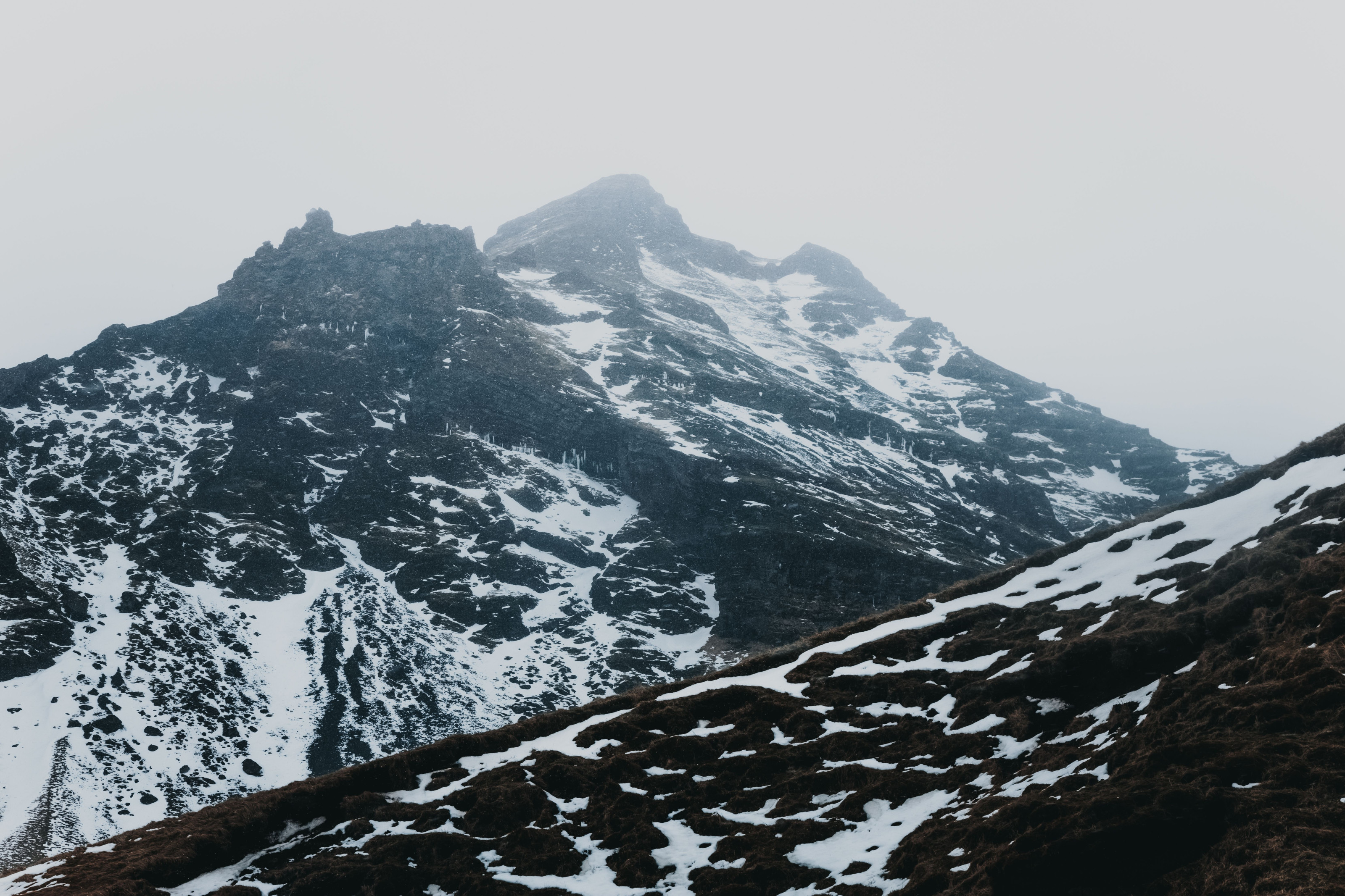 Rugged mountain peaks dusted with snow rise through drifting mist.