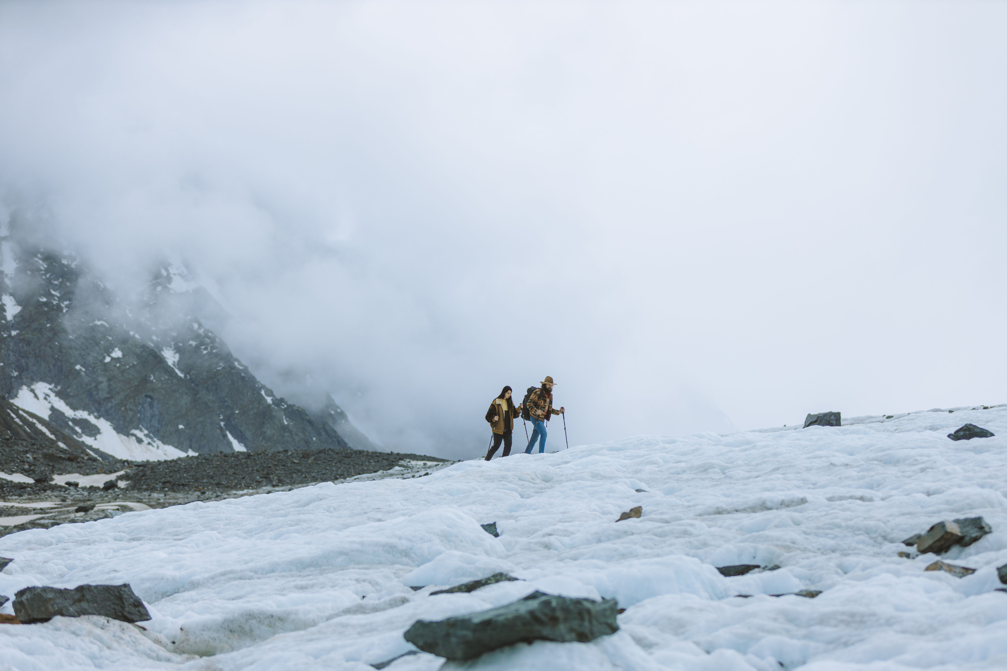 Two trekkers crossing a snow-covered mountain ridge wrapped in fog.